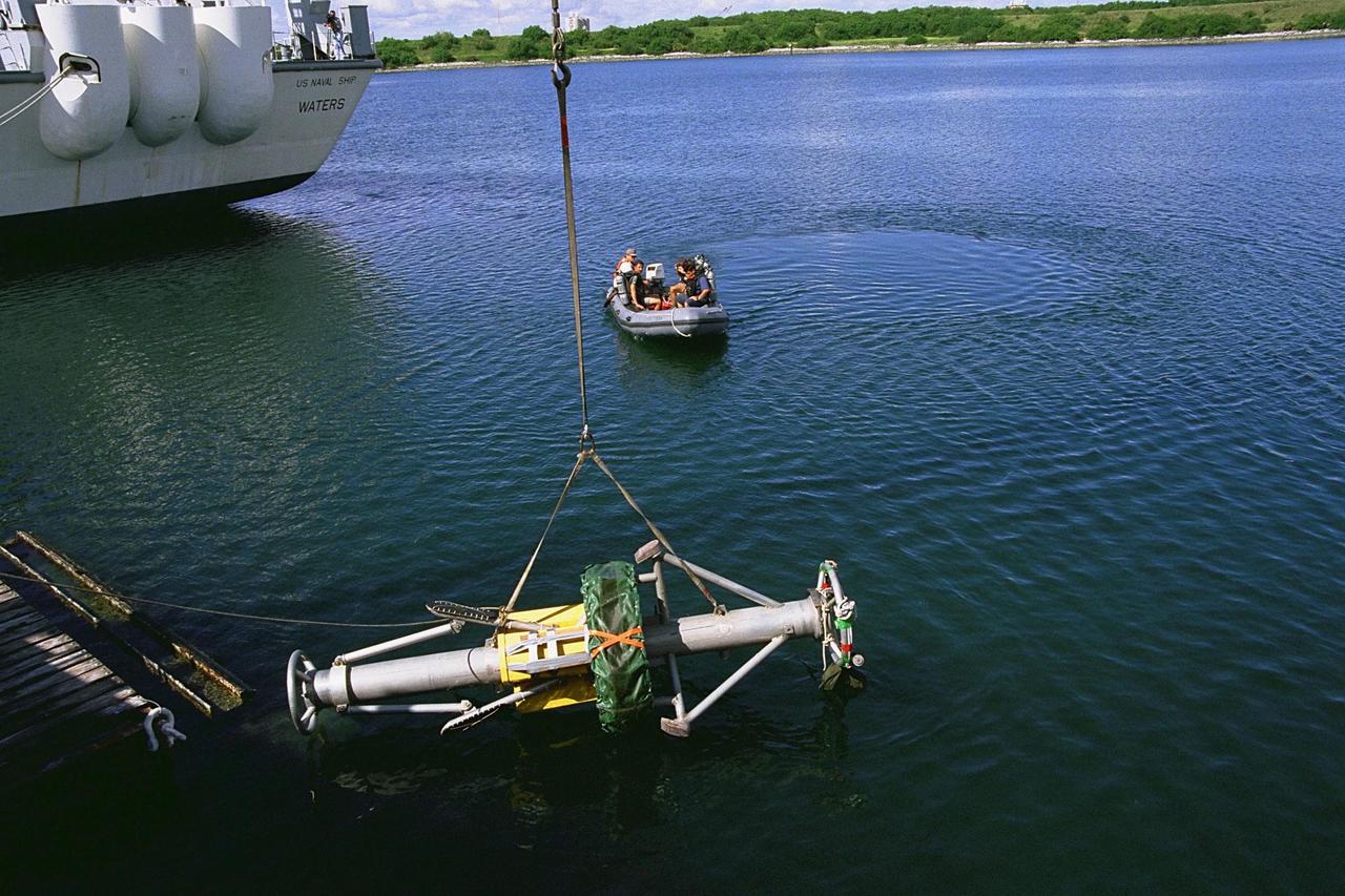KENNEDY SPACE CENTER, FLA. -- As scuba divers stand by, a Diver Operated Plug (DOP) is lowered into the water at the Trident Pier at Port Canaveral during a test of the unmanned robotic submersible recovery system, known as Max Rover. Kennedy Space Center's solid rocket booster (SRB) retrieval team and Advanced Systems Development laboratory staff hope that the new robotic technology will make the process of inserting the plug into spent SRBs safer and less strenuous. Currently, scuba divers manually insert the DOP into the aft nozzle of a jettisoned SRB 60 to 70 feet below the surface of the Atlantic Ocean. After the plug is installed, water is pumped out of the booster allowing it to float horizontally. It is then towed back to Hangar AF at Cape Canaveral Air Station for refurbishment. Deep Sea Systems of Falmouth, Mass., built the submersible for NASA
