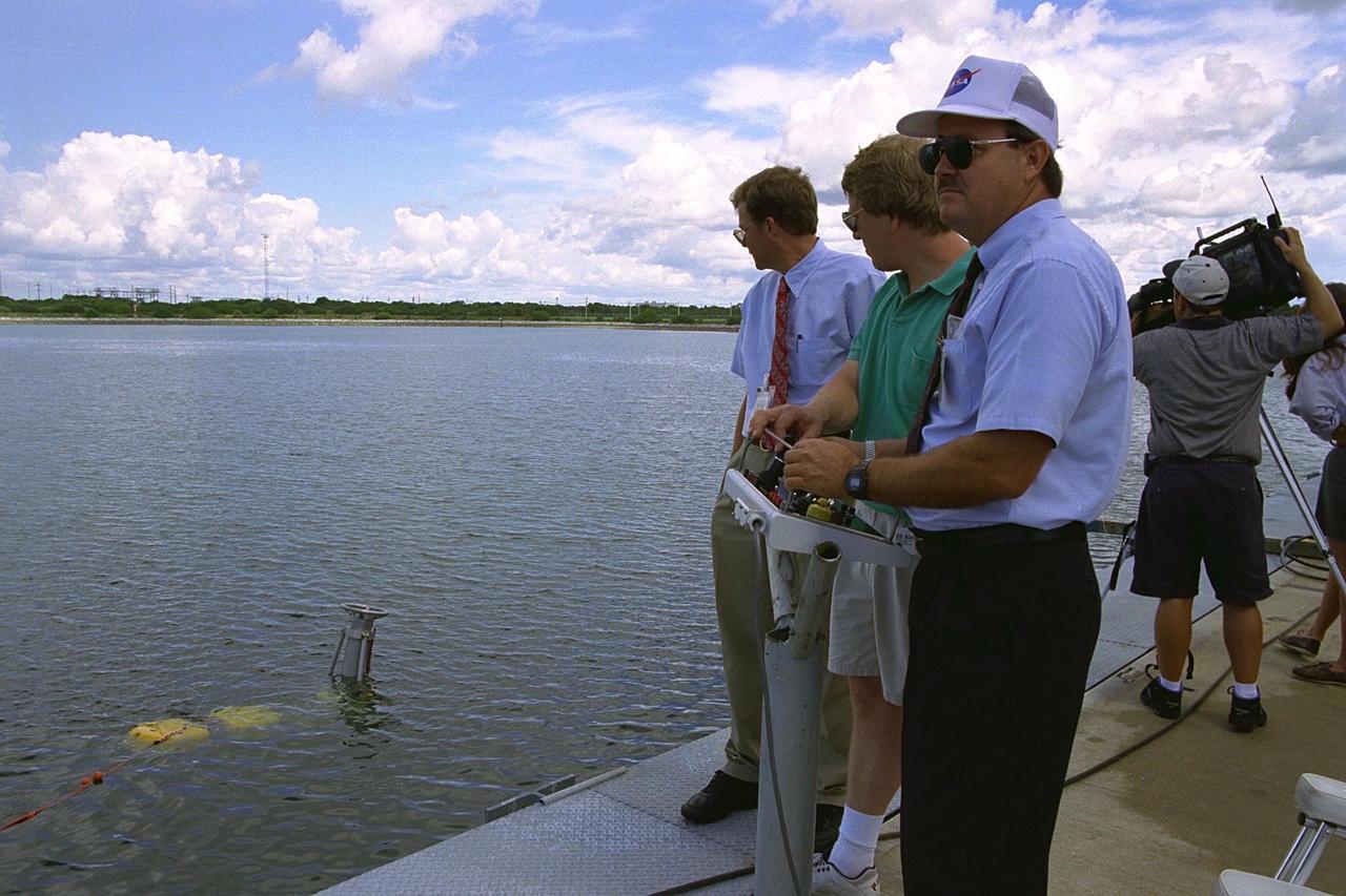 KENNEDY SPACE CENTER, FLA. -- Thomas Lippitt of NASA's Advanced Systems Development (ASD) laboratory observes robotic operations as Chris Nicholson, owner of Deep Sea Systems, and Bill Jones of NASA's ASD laboratory operate the unmanned robotic submersible recovery system, known as Max Rover, during a test of the system at the Trident Pier at Port Canaveral. The submersible is seen in the water with the Diver Operated Plug (DOP). Kennedy Space Center's solid rocket booster (SRB) retrieval team and ASD laboratory staff hope that the new robotic technology will make the process of inserting the plug safer and less strenuous. Currently, scuba divers manually insert the DOP into the aft nozzle of a jettisoned SRB 60 to 70 feet below the surface of the Atlantic Ocean. After the plug is installed, water is pumped out of the booster allowing it to float horizontally. It is then towed back to Hangar AF at Cape Canaveral Air Station for refurbishment. Deep Sea Systems of Falmouth, Mass., built the submersible for NASA