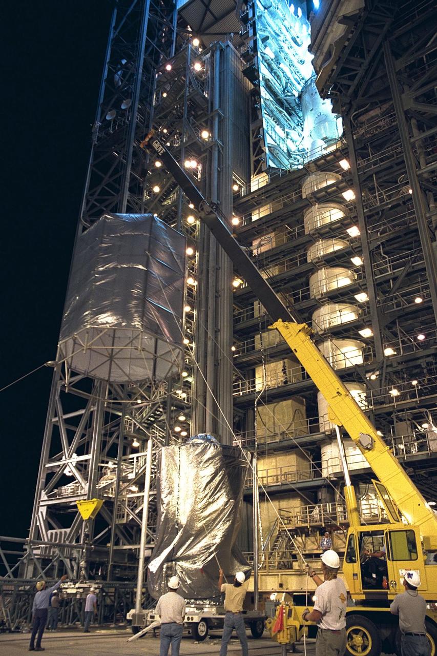 A crane lowers a protective transportation cover over the Cassini spacecraft, with its attached Huygens probe, at Launch Pad 40 at Cape Canaveral Air Station for the spacecraft’s return trip to the Payload Hazardous Servicing Facility (PHSF). Damage to thermal insulation was discovered inside Huygens from an abnormally high flow of conditioned air. Further internal inspection, insulation repair and a cleaning of the probe are now required. Mission managers are targeting a mid-October launch date after Cassini returns to the pad and is once again placed atop its Titan IVB expendable launch vehicle. Cassini will explore the Saturnian system, including the planet’s rings, while the Huygens probe will explore the moon Titan
