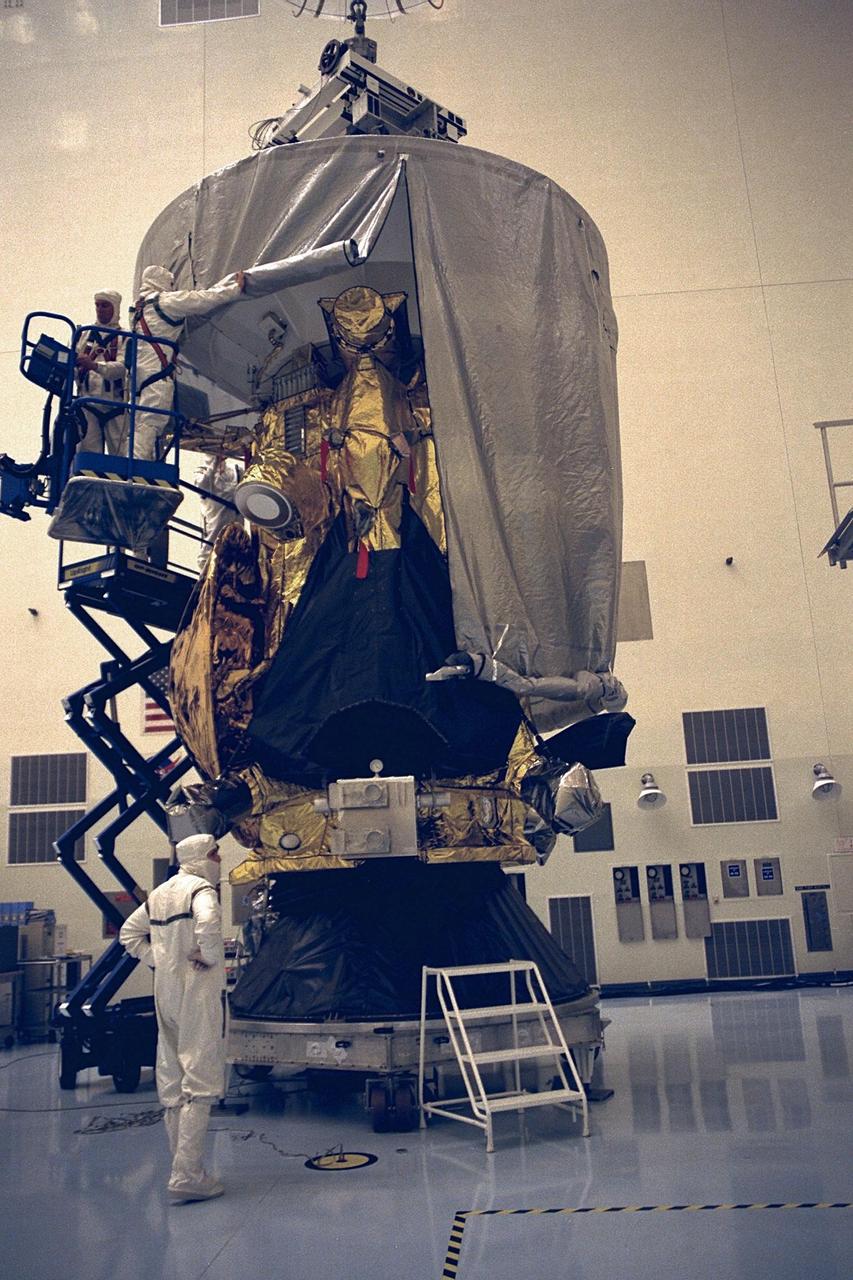Workers in the Payload Hazardous Servicing Facility (PHSF) begin to remove a protective cover from the Cassini spacecraft with its attached Huygens probe. Damage to thermal insulation was discovered inside Huygens from an abnormally high flow of conditioned air. Further internal inspection, insulation repair and a cleaning of the probe are now required. Mission managers are targeting a mid-October launch date after Cassini returns to the pad and is once again placed atop its Titan IVB expendable launch vehicle at Launch Pad 40 at Cape Canaveral Air Station. Cassini will explore the Saturnian system, including the planet’s rings, while the Huygens probe will explore the moon Titan
