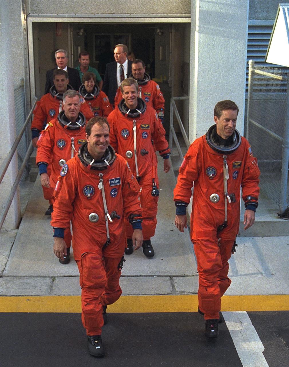 STS-86 Commander James D. Wetherbee, in foreground at right, leads the way as the next Space Shuttle crew does a practice walkout from the Operations and Checkout Building en route to Launch Pad 39A. The seven crew members are at KSC to participate in the Terminal Countdown Demonstration Test (TCDT), a dress rehearsal for launch. Pilot Michael J. Bloomfield is in foreground at left. Directly behind the pilot and commander, from left, are Mission Specialists Jean-Loup J.M. Chretien of the French Space Agency, CNES, and Scott E. Parazynski. Bringing up the rear, from left, are Mission Specialists David A. Wolf, Wendy B. Lawrence and Vladimir Georgievich Titov of the Russian Space Agency. STS-86 will be the seventh docking of the Space Shuttle with the Russian Space Station Mir. After the docking, Wolf will transfer to the Mir 24 crew, replacing U.S. astronaut C. Michael Foale, who arrived there during the last docking mission, STS-85, in May. The STS-86 launch aboard Atlantis is targeted for Sept. 25