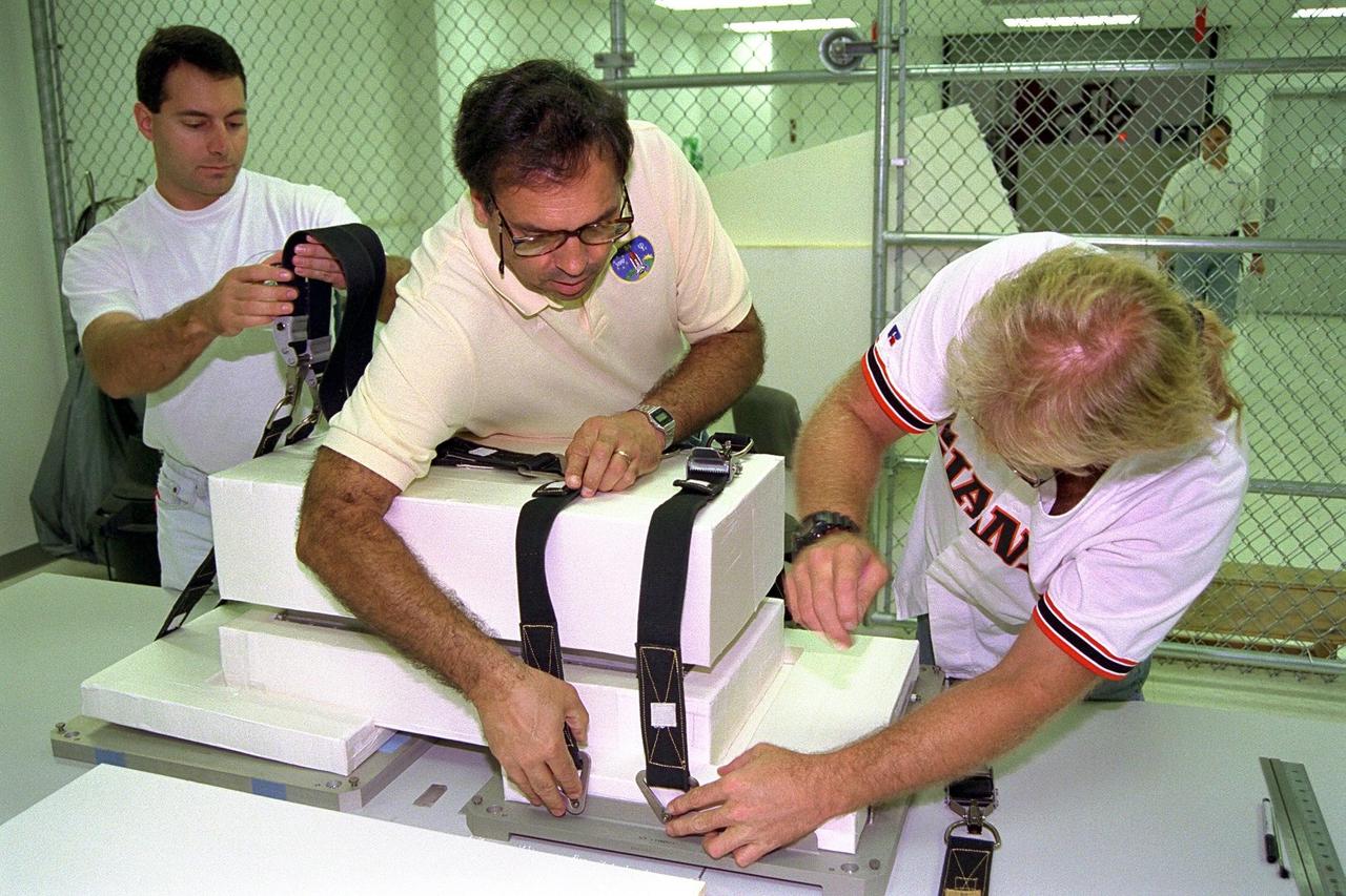 Boeing technicians, from right, John Pearce Jr., Mike Vawter and Rob Ferraro prepare a Russian replacement computer for stowage aboard the Space Shuttle Atlantis shortly before the scheduled launch of Mission STS-86, slated to be the seventh docking of the Space Shuttle with the Russian Space Station Mir. The preparations are being made at the SPACEHAB Payload Processing Facility in Cape Canaveral. The last-minute cargo addition requested by the Russians will be mounted on the aft bulkhead of the SPACEHAB Double Module, which is being used as a pressurized cargo container for science/logistical equipment and supplies that will be exchanged between Atlantis and the Mir. Using the Module Vertical Access Kit (MVAC), technicians will be lowered inside the module to install the computer for flight. Liftoff of STS-86 is scheduled Sept. 25 at 10:34 p.m. from Launch Pad 39A