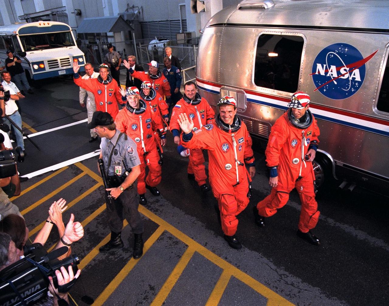 STS-86 crew members smile and wave to the crowd of press representatives, KSC employees and other well-wishers as they prepare to board the astronaut van, at right, after departing from the Operations and Checkout Building. Leading the way are Pilot Michael J. Bloomfield, at left, and Commander James D. Wetherbee. Mission Specialists David A. Wolf, at left, and Vladimir Georgievich Titov of the Russian Space Agency are directly behind them, followed by Mission Specialist Wendy B. Lawrence, at center. Bringing up the rear are Mission Specialists Scott E. Parazynski, at left, and Jean-Loup J.M. Chretien of the French Space Agency, CNES. The seven-member crew is en route to Launch Pad 39A, where the Space Shuttle Atlantis awaits liftoff on a planned 10-day mission slated to be the seventh docking of the Space Shuttle and the Russian Space Station Mir. Wolf is scheduled to transfer to the Mir 24 crew for an approximate four-month stay aboard the Russian space station. He will replace U.S. astronaut C. Michael Foale, who will return to Earth aboard Atlantis with the remainder of the STS-86 crew