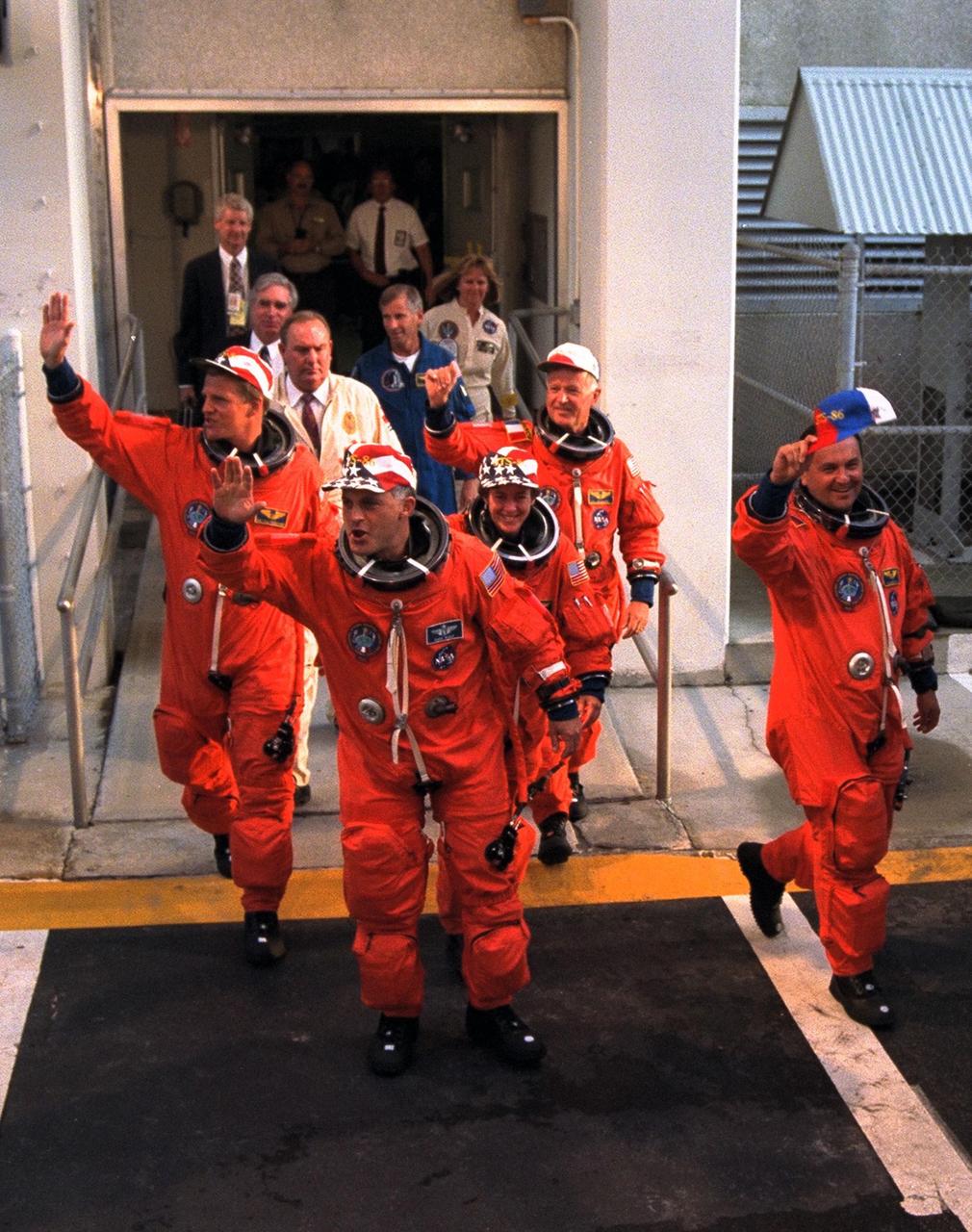 The five STS-86 mission specialists wave to the crowd of press representatives, KSC employees and other well-wishers as they depart from the Operations and Checkout Building. The three U.S. mission specialists (and their nicknames for this flight) are, from left, "too tall" Scott E. Parazynski, "just right" David A. Wolf and "too short" Wendy B. Lawrence. The two mission specialists representing foreign space agencies are Vladimir Georgievich Titov of the Russian Space Agency, in foreground at right, and Jean-Loup J.M. Chretien of the French Space Agency, CNES, in background at right. Commander James D. Wetherbee and Pilot Michael J. Bloomfield are out of the frame. STS-86 is slated to be the seventh docking of the Space Shuttle with the Russian Space Station Mir. Wolf is scheduled to transfer to the Mir 24 crew for an approximate four-month stay aboard the Russian space station. Parazynski and Lawrence were withdrawn from training for an extended stay aboard the Mir Parazynski because he was too tall to fit safely in a Russian Soyuz spacecraft, and Lawrence because she was too short to fit into a Russian spacewalk suit. The crew is en route to Launch Pad 39A, where the Space Shuttle Atlantis awaits liftoff on the planned 10-day mission