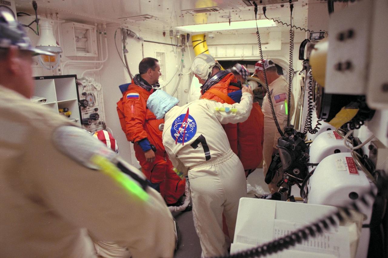 STS-86 Mission Specialist Jean-Loup J.M. Chretien, in orange launch and entry suit at right, and Mission Specialist Vladimir Georgievich Titov prepare to enter the Space Shuttle Atlantis at Launch Pad 39A, with the assistance of white room closeout crew members, including suit technician Valarie McNeal, at center