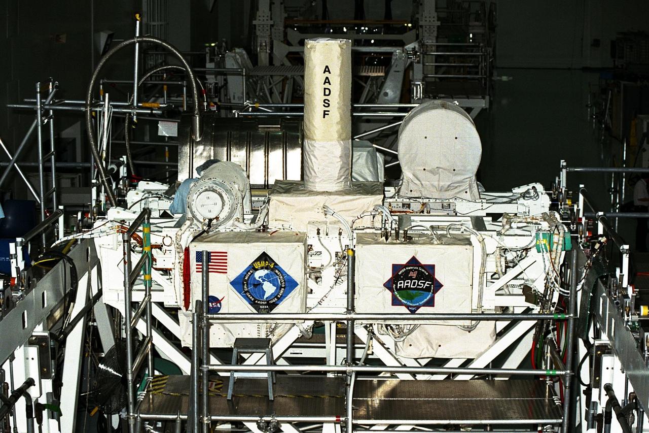 United States Microgravity Payload-4 (USMP-4) experiments are prepared to be flown on Space Shuttle mission STS-87 in the Space Station Processing Facility at Kennedy Space Center (KSC). Seen in the foreground at left is the USMP-4 logo with the acronyms of its experiments. Above the American flag at left is the MEPHISTO experiment, a cooperative American and French investigation of the fundamentals of crystal growth. The large white vertical cylinder in the center of the photo is the Advanced Automated Directional Solidification Furnace (AADSF), which is a sophisticated materials science facility used for studying a common method of processing semiconductor crystals called directional solidification. The white horizontal tube to the right is the Isothermal Dendritic Growth Experiment (IDGE), which will be used to study the dendritic solidification of molten materials in the microgravity environment. All USMP-4 experiments are scheduled for launch aboard STS-87 on Nov. 19 from KSC