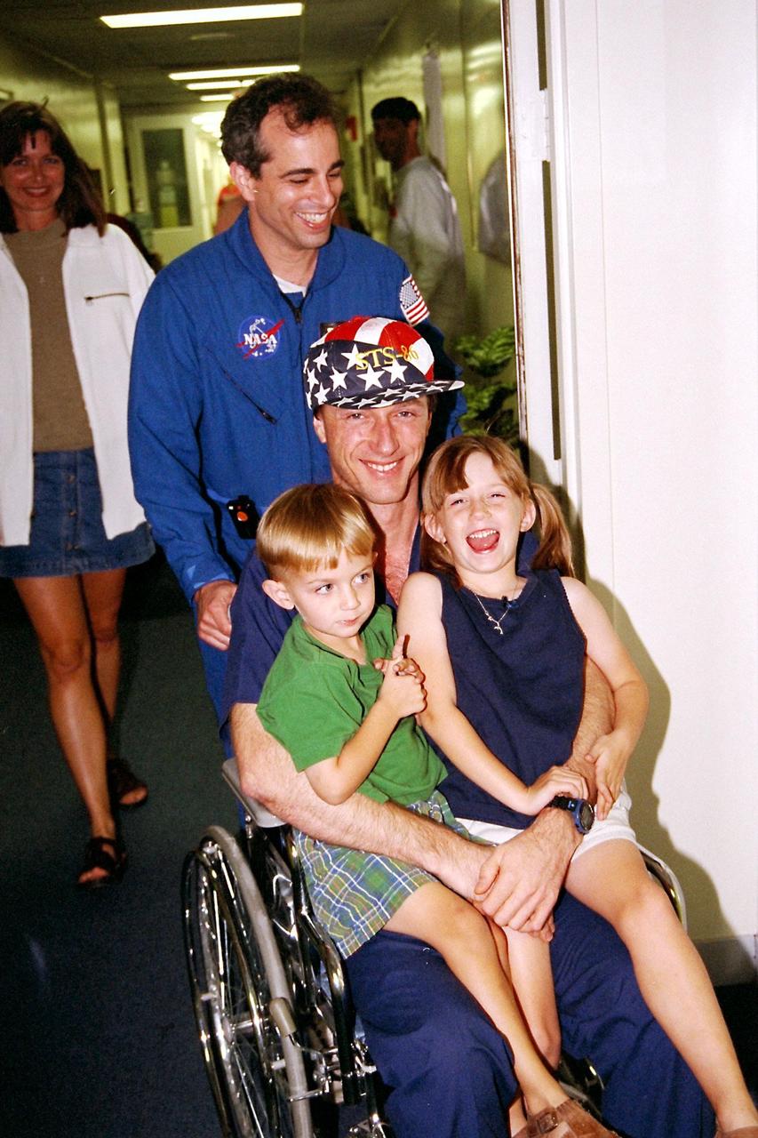 Astronaut C. Michael Foale gets extra-special care back on Earth from his family and his flight physician after an approximate four-and-a-half-month stay aboard the Russian Space Station Mir. Dr. Terry Tadeo, a NASA physician who has been monitoring the astronaut’s health during his stay on the Mir, pushes the wheelchair holding Foale and the space flyer’s two children, 3-year-old Ian and 5-year-old Jenna, through the astronaut crew quarters of the Operations and Checkout Building. Foale’s wife, Rhonda, is in background at left. Foale’s family was at KSC for the late-night reunion after the Oct. 6 landing of the Space Shuttle orbiter Atlantis on the STS-86 mission. Foale, a member of the Mir 24 crew, was dropped off on the Russian space station during the STS-84 mission in mid-May. He joined the STS-86 crew aboard Atlantis for the return trip to Earth. STS-86 was the seventh docking of the Space Shuttle with the Mir. STS-86 Mission Specialist David A. Wolf replaced Foale on the Russian station