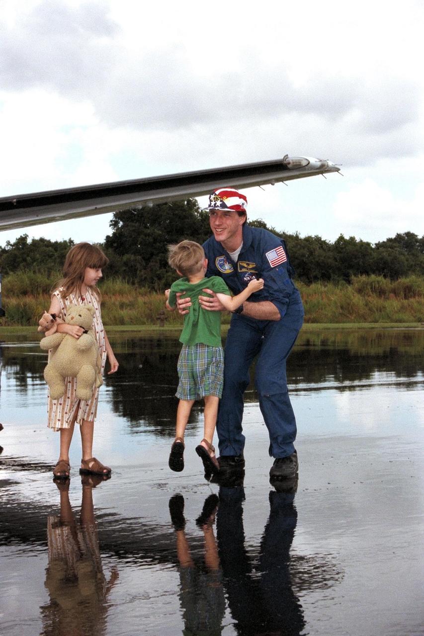 Still celebrating his recent homecoming and reunion with his family, astronaut C. Michael Foale picks up his 3-year-son Ian, while his 5-year-old daughter, Jenna, stands by at the Skid Strip on Cape Canaveral Air Station. They are scheduled to depart shortly for the astronauts’ home base at Johnson Space Center in Houston, Texas. Foale spent approximately four-and-a-half months on the Russian Space Station Mir. He returned to Earth on Oct. 6 aboard the Space Shuttle orbiter Atlantis at the conclusion of the STS-86 mission. STS-86 was the seventh docking of the Space Shuttle with the Mir. Foale was replaced on the Mir by STS-86 Mission Specialist David A. Wolf