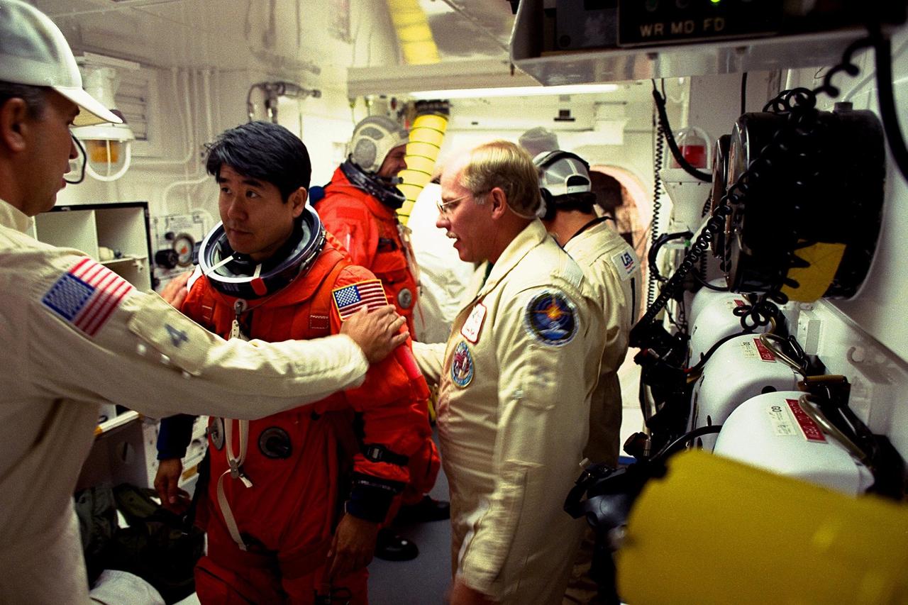 STS-87 Mission Specialist Takao Doi, Ph.D., of the National Space Development Agency of Japan, is assisted with his ascent and re-entry flight suit by Dave Law, USA mechanical technician, in the white room at Launch Pad 39B as Dr. Doi prepares to enter the Space Shuttle orbiter Columbia on launch day. At right wearing glasses is Danny Wyatt, NASA quality assurance specialist. STS-87 is the fourth flight of the United States Microgravity Payload and Spartan-201. The 16-day mission will include a spacewalk by Dr. Doi and Mission Specialist Winston Scott
