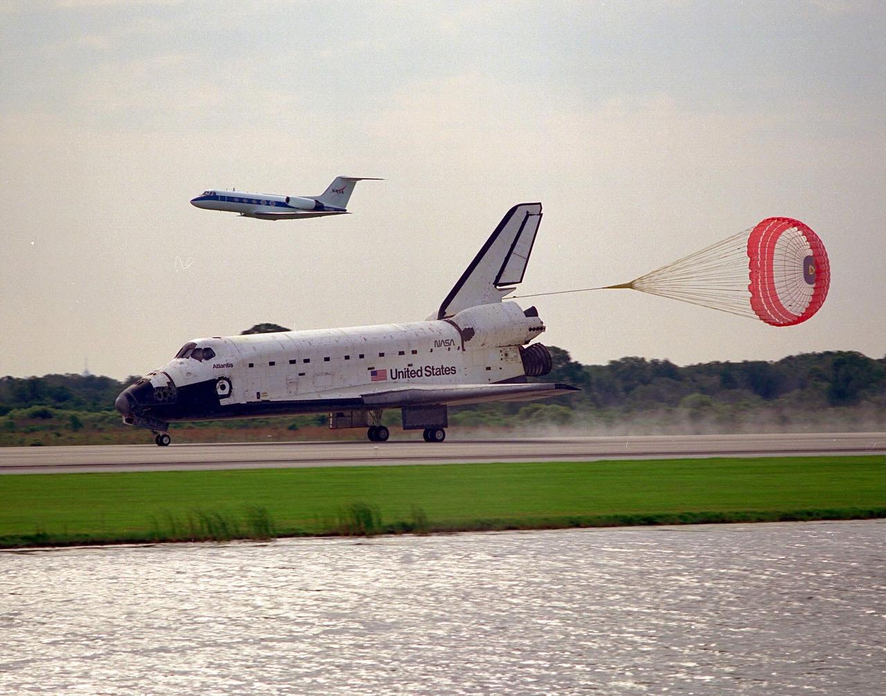The Space Shuttle orbiter Atlantis, with its drag chute deployed, rolls out on Runway 33 of KSC’s Shuttle Landing Facility at the conclusion of the nine-day STS-84 mission. The Shuttle Training Aircraft piloted by astronaut Kenneth D. Cockrell, acting deputy chief of the Astronaut Office, is flying above Atlantis. Main gear touchdown was at 9:27:44 EDT on May 24, 1997. The first landing opportunity was waved off because of low cloud cover. It was the 37th landing at KSC since the Shuttle program began in 1981, and the eighth consecutive landing at KSC. STS-84 was the sixth of nine planned dockings of the Space Shuttle with the Russian Space Station Mir. Atlantis was docked with the Mir for five days. STS-84 Mission Specialist C. Michael Foale replaced astronaut and Mir 23 crew member Jerry M. Linenger, who has been on the Russian space station since Jan. 15. Linenger returned to Earth on Atlantis with the rest of the STS-84 crew, Mission Commander Charles J. Precourt, Pilot Eileen Marie Collins, and Mission Specialists Carlos I. Noriega, Edward Tsang Lu, Elena V. Kondakova of the Russian Space Agency and JeanFrancois Clervoy of the European Space Agency. Foale is scheduled to remain on the Mir for approximately four months, until he is replaced by STS-86 crew member Wendy B. Lawrence in September. Besides the docking and crew exchange, STS-84 included the transfer of more than 7,300 pounds of water, logistics and science experiments and hardware to and from the Mir. Scientific experiments conducted during the STS-84 mission, and scheduled for Foale’s stay on the Mir, are in the fields of advanced technology, Earth sciences, fundamental biology, human life sciences, International Space Station risk mitigation, microgravity sciences and space sciences