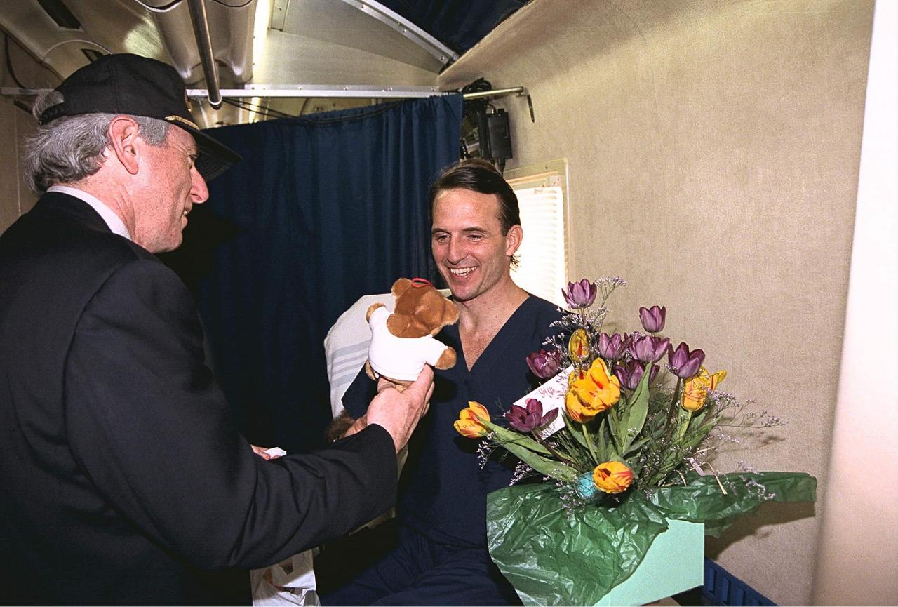 NASA Administrator Daniel Goldin presents some gifts to returning astronaut Jerry M. Linenger, who spent the last four months on the Russian Space Station Mir. Goldin met with Linenger in the Crew Transport Vehicle shortly after the Space Shuttle orbiter Atlantis landed on Runway 33 of KSC’s Shuttle Landing Facility at the conclusion of the nine-day STS-84 mission. Goldin gave the astronaut flowers for Linenger’s wife, Kathryn; a stuffed bear for their 18-month-old son, John; and a rattle for their unborn child who is due next month. STS-84 was the sixth of nine planned dockings of the Space Shuttle with the Mir. Mir 23 crew member Linenger was replaced on the Russian space station by STS-84 Mission Specialist C. Michael Foale