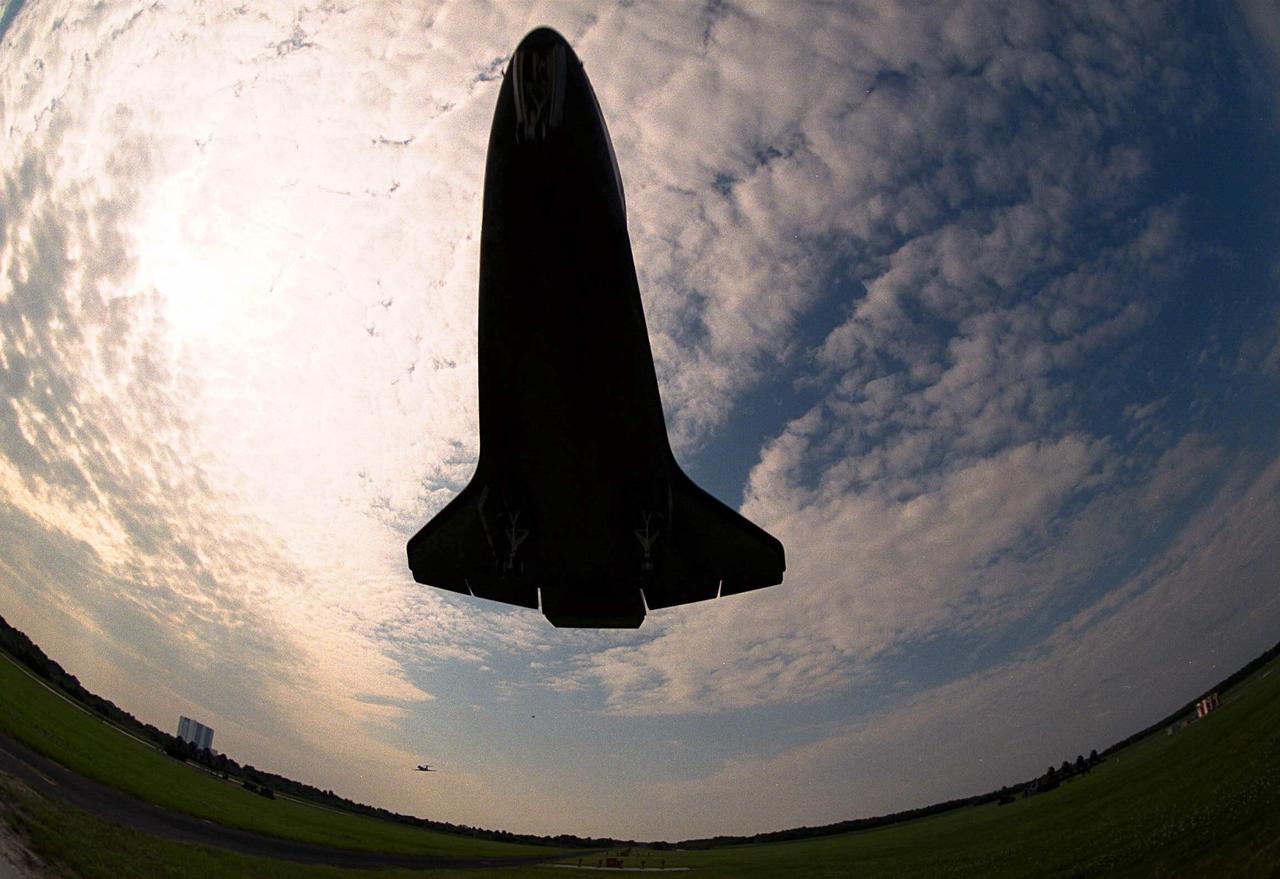 This unusual view of the underside of the Space Shuttle orbiter Atlantis shortly before landing was taken by a fish-eye camera lens from KSC’s Shuttle Landing Facility. The Vehicle Assembly Building is in the background at left. The Shuttle Training Aircraft can be seen in the distance, at center. Atlantis is wrapping up its nine-day STS-84 mission, which was the sixth docking of the Space Shuttle with the Russian Space Station Mir. Atlantis was docked with the Mir for five days. STS-84 Mission Specialist C. Michael Foale replaced astronaut and Mir 23 crew member Jerry M. Linenger, who has been on the Russian space station since Jan. 15. Linenger is returning to Earth on Atlantis with the rest of the STS-84 crew, Mission Commander Charles J. Precourt, Pilot Eileen Marie Collins, and Mission Specialists Carlos I. Noriega, Edward Tsang Lu, Elena V. Kondakova of the Russian Space Agency and Jean-Francois Clervoy of the European Space Agency. Foale is scheduled to remain on the Mir for approximately four months, until he is replaced by STS-86 crew member Wendy B. Lawrence in September. Besides the docking and crew exchange, STS-84 included the transfer of more than 7,300 pounds of water, logistics and science experiments and hardware to and from the Mir. Scientific experiments conducted during the STS-84 mission, and scheduled for Foale’s stay on the Mir, are in the fields of advanced technology, Earth sciences, fundamental biology, human life sciences, International Space Station risk mitigation, microgravity sciences and space sciences