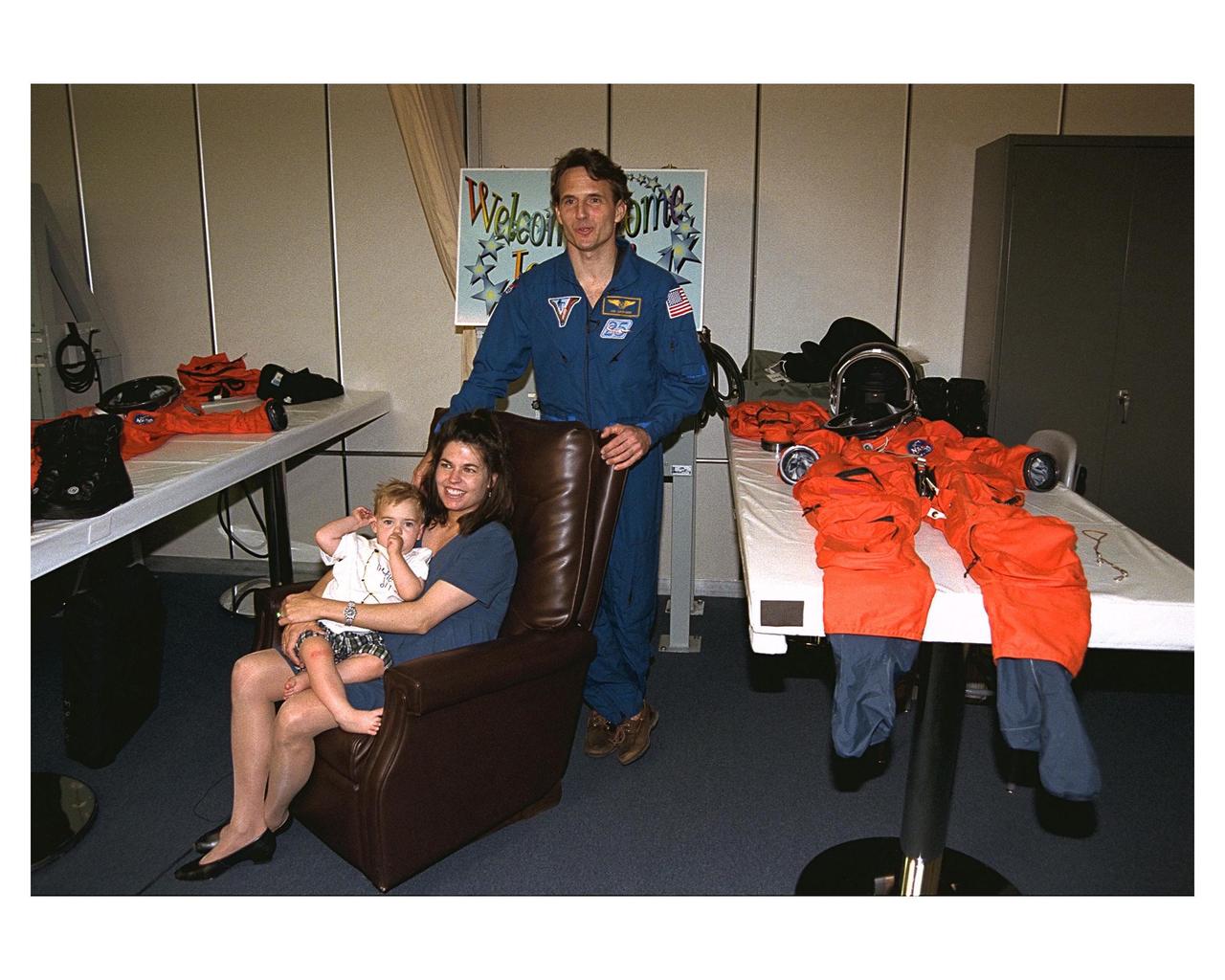 Astronaut and recent Mir 23 crew member Jerry M. Linenger, standing, reunites with his wife, Kathryn, and their 18-month-old son, John, in the astronaut suit-up room in the Operations and Checkout Building. Kathryn Linenger is expecting their second child next month. Linenger just returned to Earth after a four-month stay on the Russian Space Station Mir. He flew back on Atlantis with six other members of the STS-84 crew, who conducted the sixth Space Shuttle docking with the Mir. STS-84 Mission Specialist C. Michael Foale replaced Linenger on the Mir