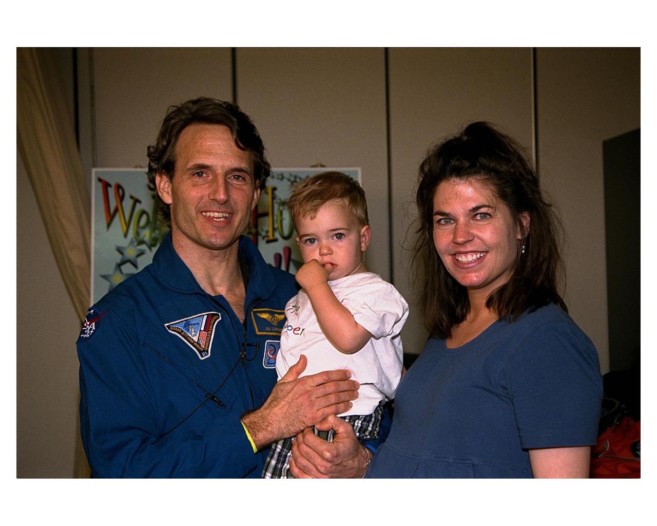 Astronaut and recent Mir 23 crew member Jerry M. Linenger poses for a photograph with his wife, Kathryn, and their 18-month-old son, John, during a family reunion in the Operations and Checkout Building. Kathryn Linenger is expecting their second child next month. Linenger just returned to Earth after a four-month stay on the Russian Space Station Mir. He flew back on Atlantis with six other members of the STS-84 crew, who conducted the sixth Space Shuttle docking with the Mir. STS-84 Mission Specialist C. Michael Foale replaced Linenger on the Mir