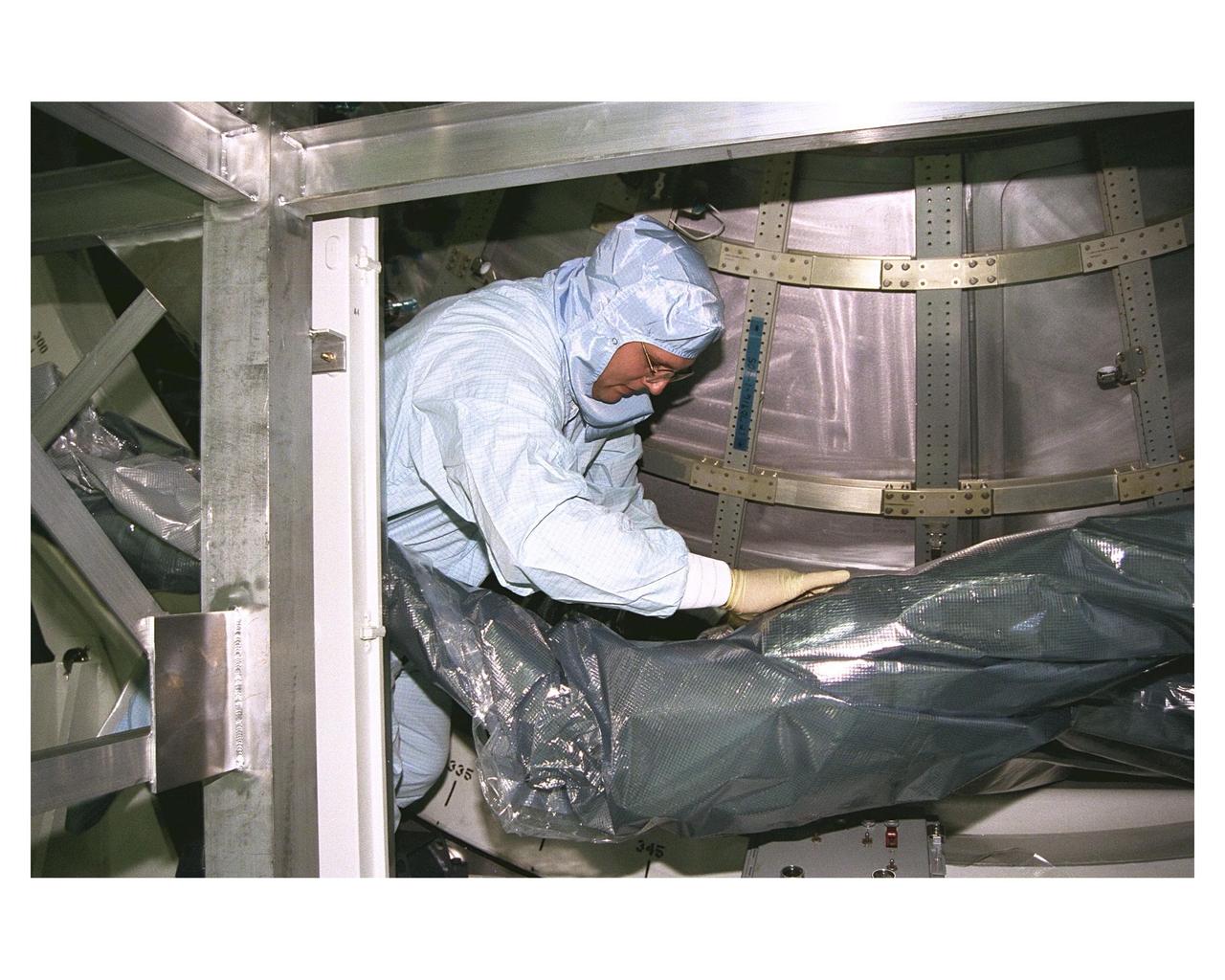 A KSC payloads processing employee removes a protective sheath part of the Node 1 in its work stand in the Space Station Processing Facility. The module is the first element of the International Space Station to be manufactured in the United States and the first scheduled to be launched on the Space Shuttle. The Node 1 is currently scheduled to lift off aboard the Space Shuttle Endeavour in July 1998, along with Pressurized Mating Adapters (PMAs) 1 and 2. The 18-foot-in-diameter, 22-foot-long aluminum module was manufactured by the Boeing Co. at Marshall Space Flight Center. Once in space, the Node 1 will function as a connecting passageway to the living and working areas of the International Space Station. It has six hatches that will serve as docking ports to the U.S. laboratory module, U.S. habitation module, an airlock and other space station elements
