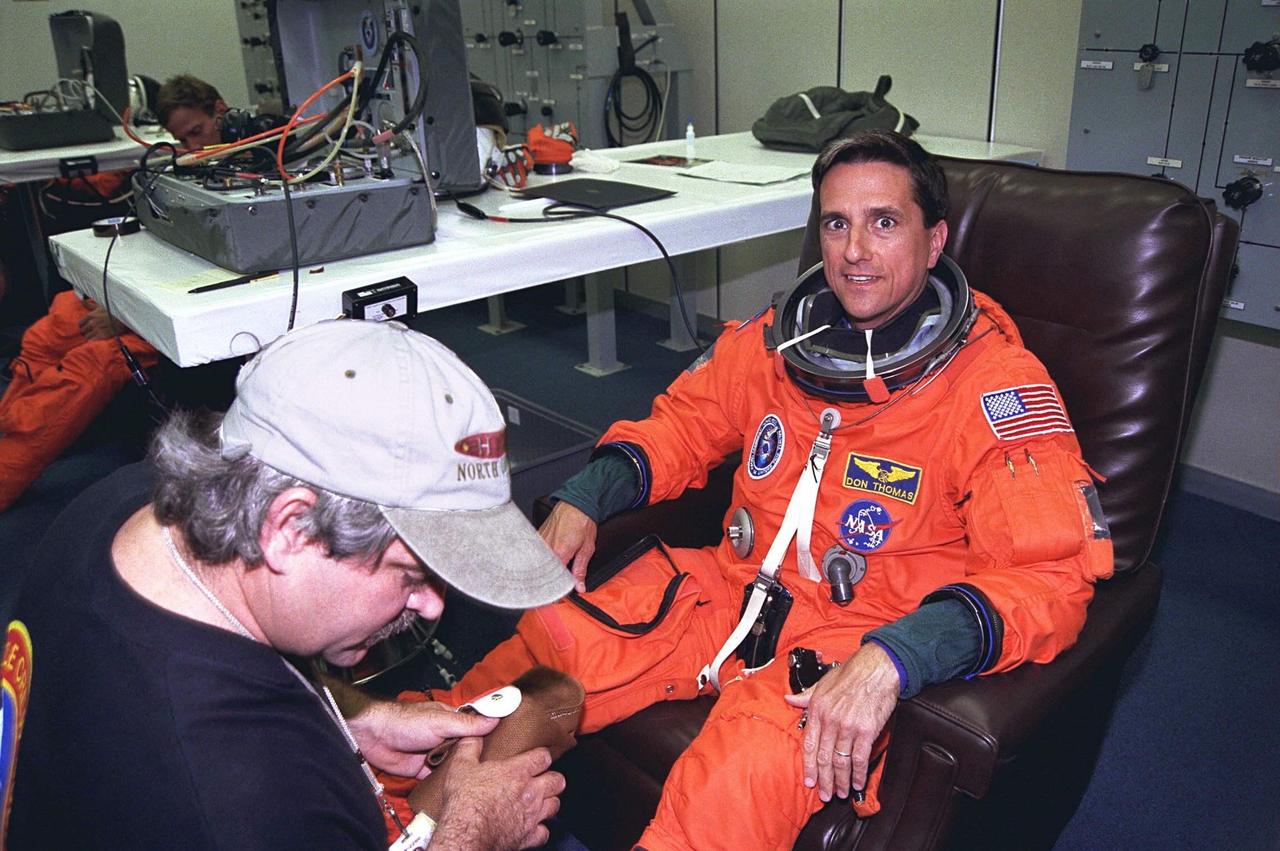 STS-94 Mission Specialist Donald A. Thomas  smiles as a suit technician helps him into his launch/entry suit in the Operations and  Checkout (O&C) Building. He has flown on STS-83, STS-70 and STS-65. He holds a  doctorate in materials science and has been the Principal Investigator for a Space Shuttle  crystal growth experiment. Because of his background in materials science, Thomas will  be concentrating his efforts during the Red shift on the five experiments in this discipline  in the Large Isothermal Furnace. He also will work on  the ten materials science  investigations in the Electromagnetic Containerless Processing Facility and four that will  be measuring the effects of  microgravity and motion in the orbiter on the experiments.  Thomas and six fellow crew members will shortly depart  the O&C and head for Launch  Pad 39A, where the  Space Shuttle Columbia will lift off  during a launch window that  opens at 1:50 p.m. EDT, July 1. The launch window was opened 47 minutes early to  improve the opportunity to lift off before Florida summer rain showers reached the space  center