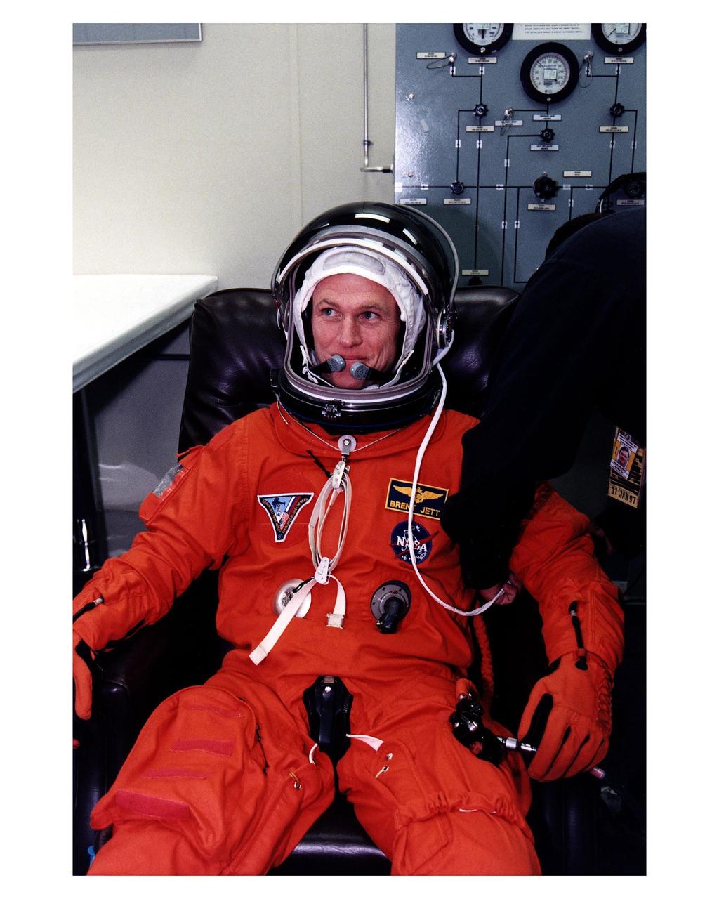 STS-81 Pilot Brent W. Jett, Jr. dons his launch/entry suit in the suitup room of the Operations and Checkout (O&C) Building. He is on his second Shuttle mission. Jett will assist with several of the 44 Risk Mitigation and Human Life Sciences experiments during the 10-day space flight and will perform the intricate flyaround maneuver of the Russian Mir space station after the Space Shuttle Atlantis undocks on flight day eight. He and five crew members will shortly depart the O&C and head for Launch Pad 39B, where the Space Shuttle Atlantis will lift off during a 7-minute window that opens at 4:27 a.m. EST, January 12