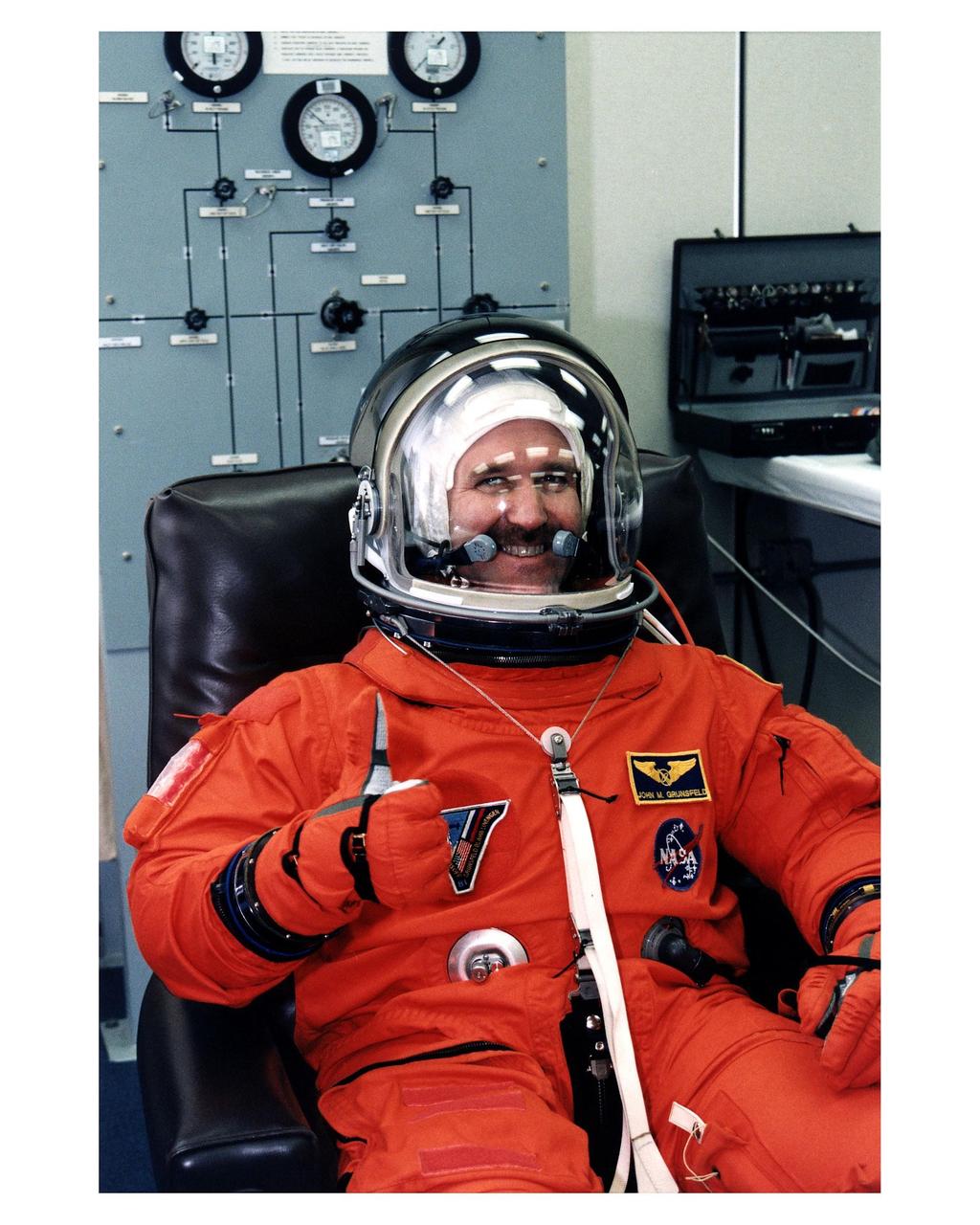 STS-81 Mission Specialist John M. Grunsfeld. gives a thumbs-up as he completes his launch/entry suitup in the Operations and Checkout (O&C) Building. He is on his second Shuttle flight and holds doctorate and master’s degrees in physics. He will be have overall responsibility for science experiments on the 7-day space flight and will watch over environmental and biological samples that will be taken on the Mir space station and returned to Earth on the Space Shuttle Atlantis. He and five crew members will shortly depart the O&C and head for Launch Pad 39B, where the Space Shuttle Atlantis will lift off during a 7-minute window that opens at 4:27 a.m. EST, January 12