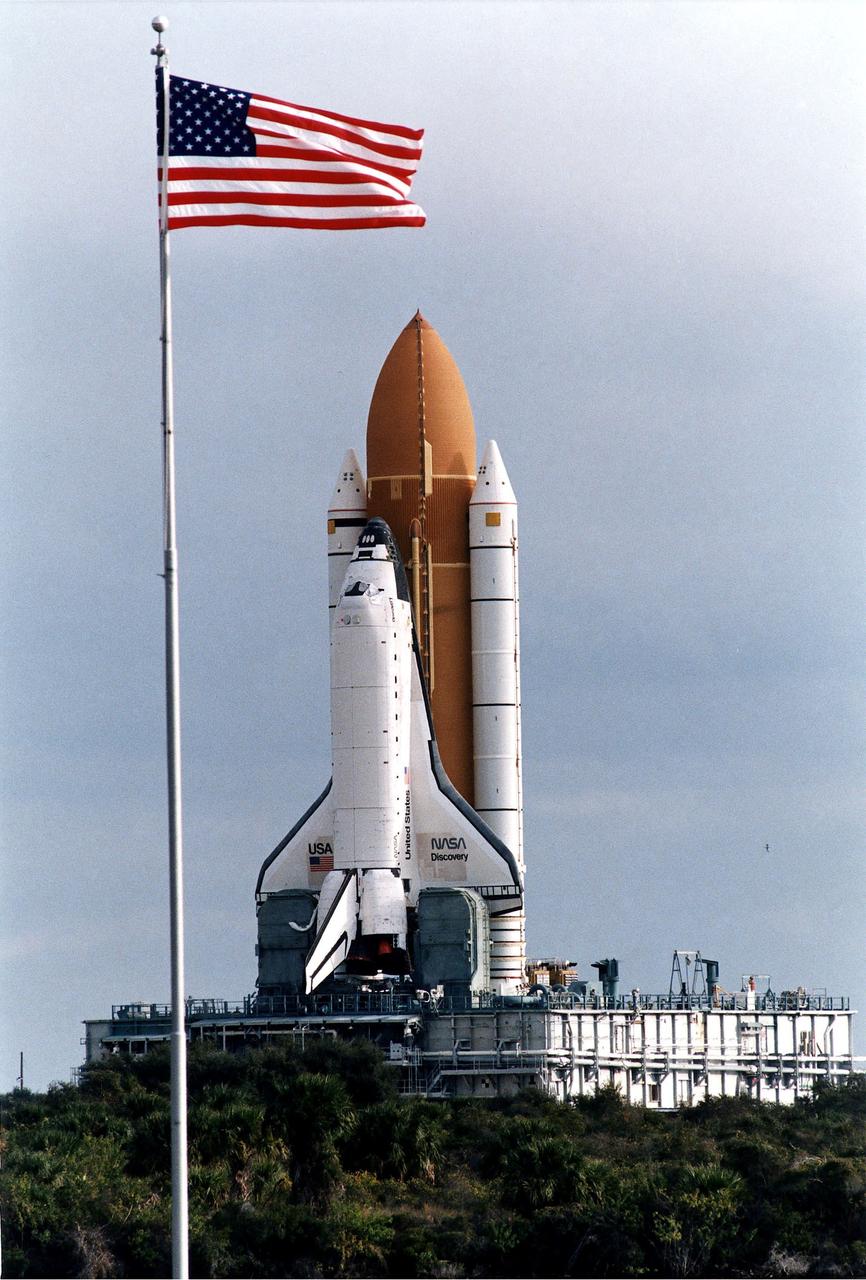 KENNEDY SPACE CENTER, FLA. -  The Space Shuttle Discovery on its Mobile Launcher Platform makes its slow 3.4-mile trek from the Vehicle Assembly Building to Launch Pad 39A in preparation for the STS-82 mission.  In the foreground is the U.S. flag at the Press Site area.  A seven-member crew will perform the second servicing of the orbiting Hubble Space Telescope (HST) during the 10-day STS-82 mission, which is targeted for a Feb. 11 liftoff.