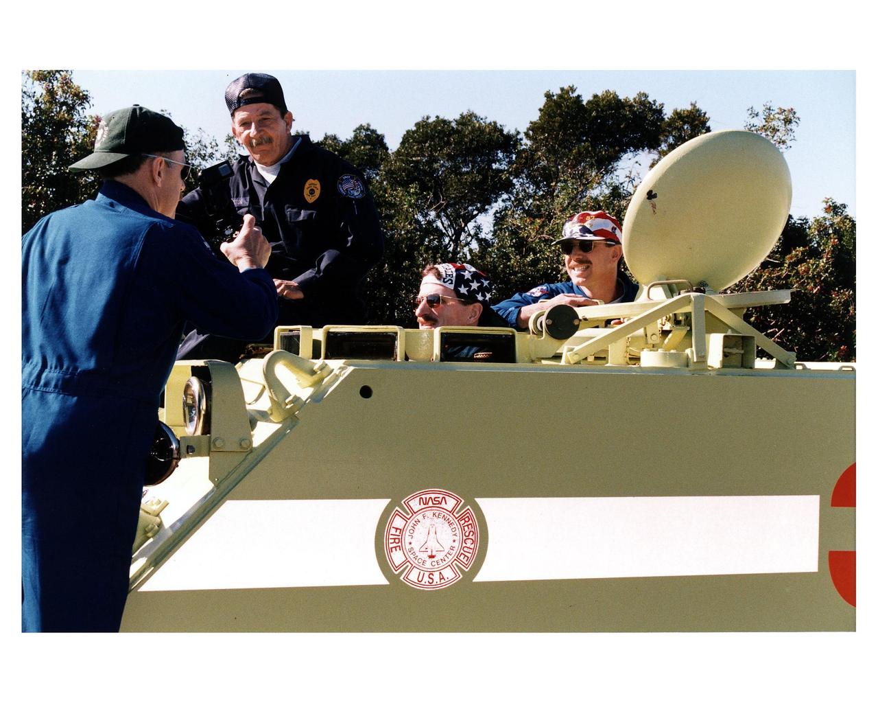 STS-82 Mission Commander, far left, takes a photograph of his fellow crew members Pilot Scott J. "Doc" Horowitz, at far right, and Mission Specialist Joseph R. "Joe" Tanner while they are training in the M-113 armored personnel carrier. George Hoggard, a training officer with KSC Fire Services, looks on. The STS-82 crew is at KSC to participate in the Terminal Countdown Demonstration Test (TCDT), a dress rehearsal for launch. The 10-day flight, which will be the second Hubble Space Telescope servicing mission, is targeted for a Feb. 11 liftoff