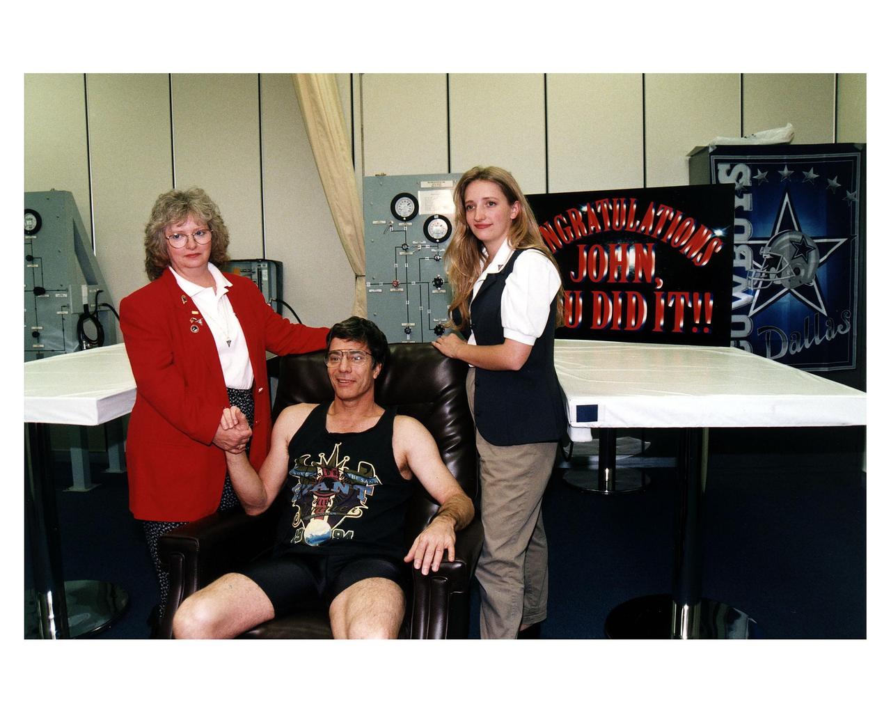 U. S. astronaut John E. Blaha poses with his wife, Brenda (left), and daughter, Carolyn (right), in the crew quarters at KSC after answering questions about his four-month stay aboard the Russian Mir space station. Blaha returned to Earth earlier today aboard the Space Shuttle orbiter Atlantis when it touched down at 9:22:44 a.m. EST Jan. 22 on Runway 33 of KSC’s Shuttle Landing Facility at the conclusion of the STS-81 mission. Blaha and the other five returning STS-81 crew members are spending the night here in the Operations and Checkout Building before returning to Johnson Space Center in Houston tomorrow morning. Blaha will undergo a two-week series of medical tests to help determine the physiological effects of his long-duration mission