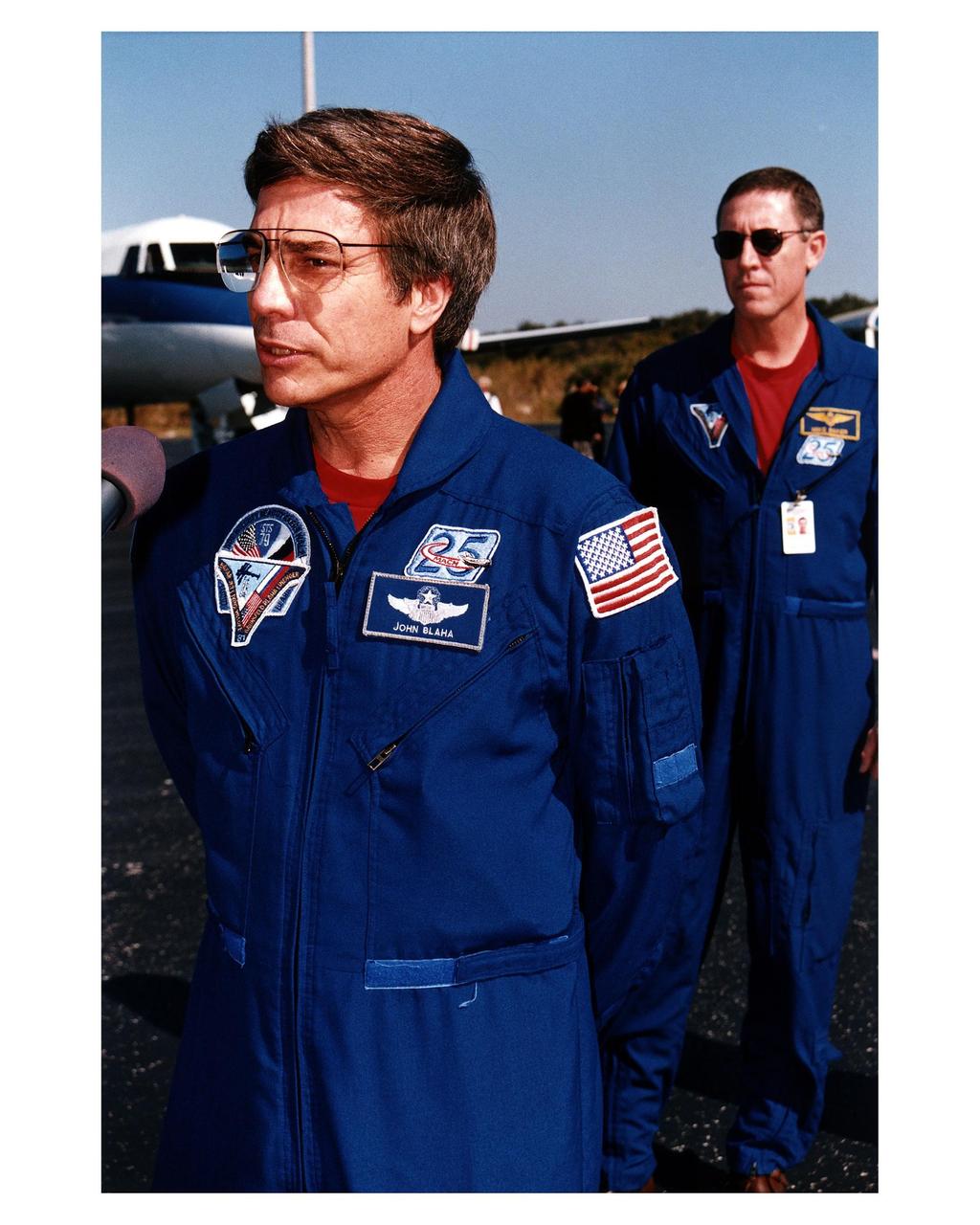 Returning NASA astronaut and former Mir 22 crew member John E. Blaha (left), addresses the news media at the Skid Strip at Cape Canaveral Air Station as he and fellow STS-81 crew members prepare to depart for Johnson Space Center Jan. 23. The crew arrived at KSC aboard the Space Shuttle Atlantis Jan. 22 to conclude the fifth Shuttle-Mir docking mission and return Blaha to Earth after four months in space. Behind Blaha is Mission Commander Michael A. Baker
