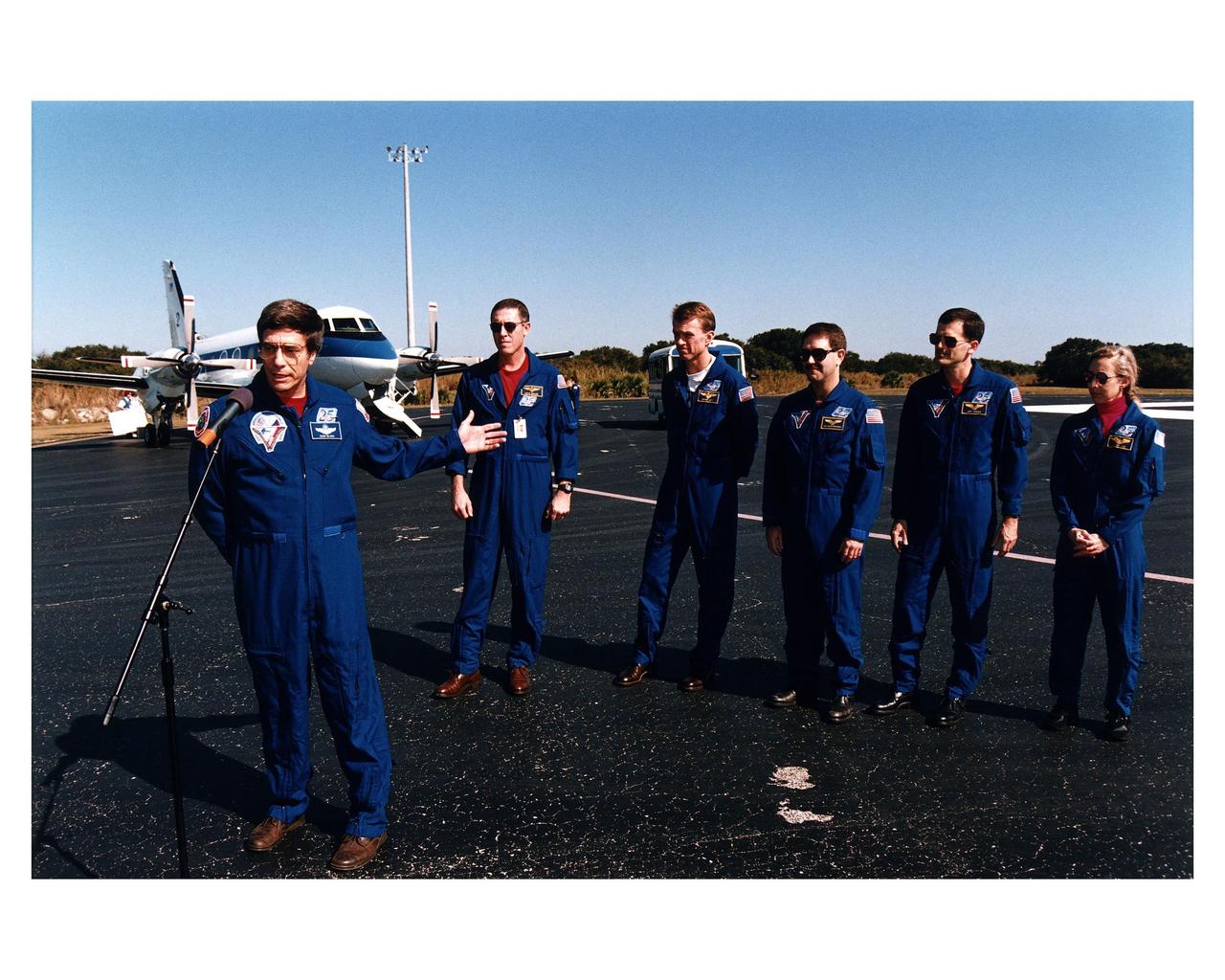 Returning NASA astronaut and former Mir 22 crew member John E. Blaha (left), gestures towards his fellow STS-81 crew members during a press conference prior to their departure for Johnson Space Center Jan. 23 from the Skid Strip at Cape Canaveral Air Station. The crew arrived at KSC aboard the Space Shuttle Atlantis Jan. 22 to conclude the fifth Shuttle-Mir docking mission and return Blaha to Earth after four months in space. Behind Blaha from the left are Mission Commander Michael A. Baker; Pilot Brent W. Jett, and Mission Specialists John M. Grunsfeld, Peter J. K. "Jeff" Wisoff and Marsha S. Ivins