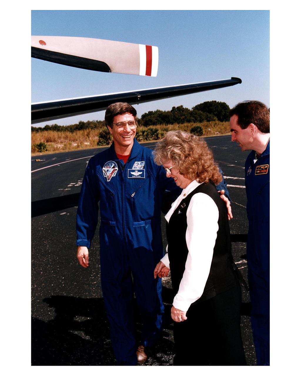 Returning NASA astronaut and former Mir 22 crew member John E. Blaha (left), puts his arm around his wife, Brenda, as they prepare to depart with the STS-81 crew for Johnson Space Center Jan. 23 from the Skid Strip at Cape Canaveral Air Station. NASA’s Patrick McGinnis is on the right. The STS-81 crew arrived at KSC aboard the Space Shuttle Atlantis Jan. 22 to conclude the fifth ShuttleMir docking mission and return Blaha to Earth after four months in space