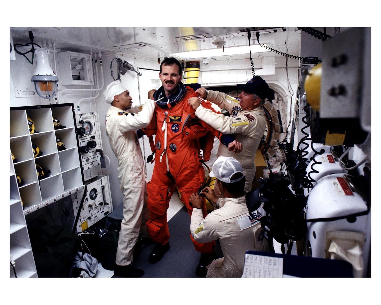 STS-82 Mission Specialist Steven L. Smith prepares to enter the Space Shuttle Discovery at Launch Pad 39A, with the assistance of white room closeout crew members Dave Law, in front; Carlous Gillis, at left; and James Davis