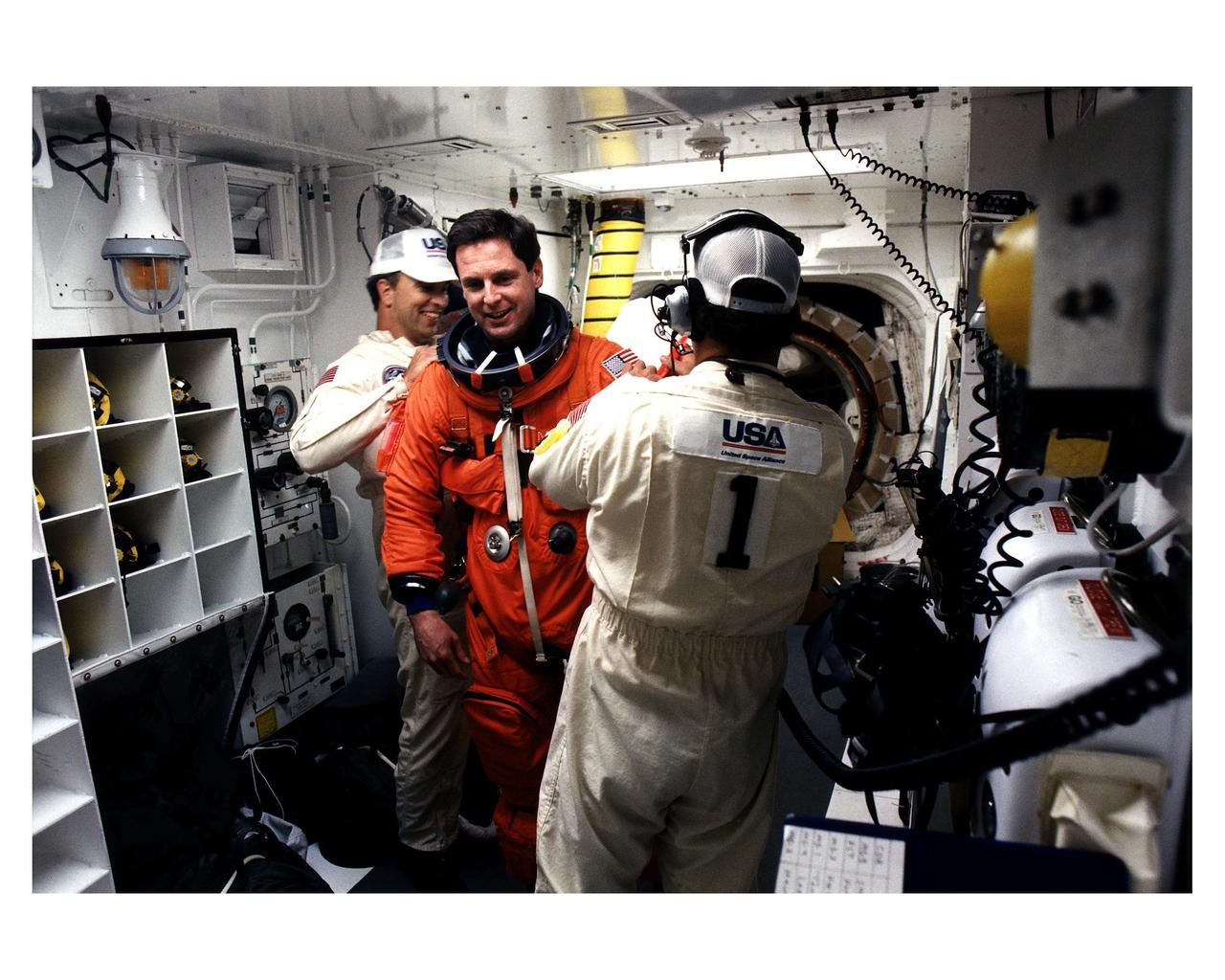 STS-82 Mission Specialist Gregory J. Harbaugh prepares to enter the Space Shuttle Discovery at Launch Pad 39A, with the assistance of white room closeout crew members Dave Law, at left, and Travis Thompson