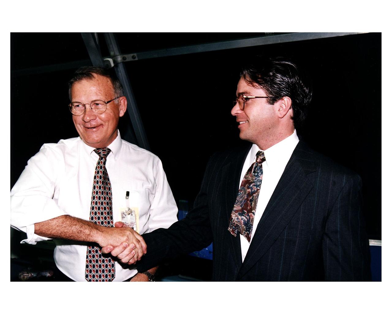 KSC Center Director Jay F. Honeycutt, at left, shakes hands with Scott Cilento, the new flow director of the Space Shuttle orbiter Discovery, in the firing room of the Launch Control Center (LCC) during the STS-82 launch of Discovery on the second Hubble Space Telescope servicing mission. This is Cilento's first launch as Discovery's flow director and Honeycutt's last launch as center director. Honeycutt plans to retire and will be succeeded by Roy D. Bridges Jr. on March 2, 1997. Cilento only has half a tie because Honeycutt just cut it, upholding the LCC tradition of cutting the tie of the person performing in a new role for the first time