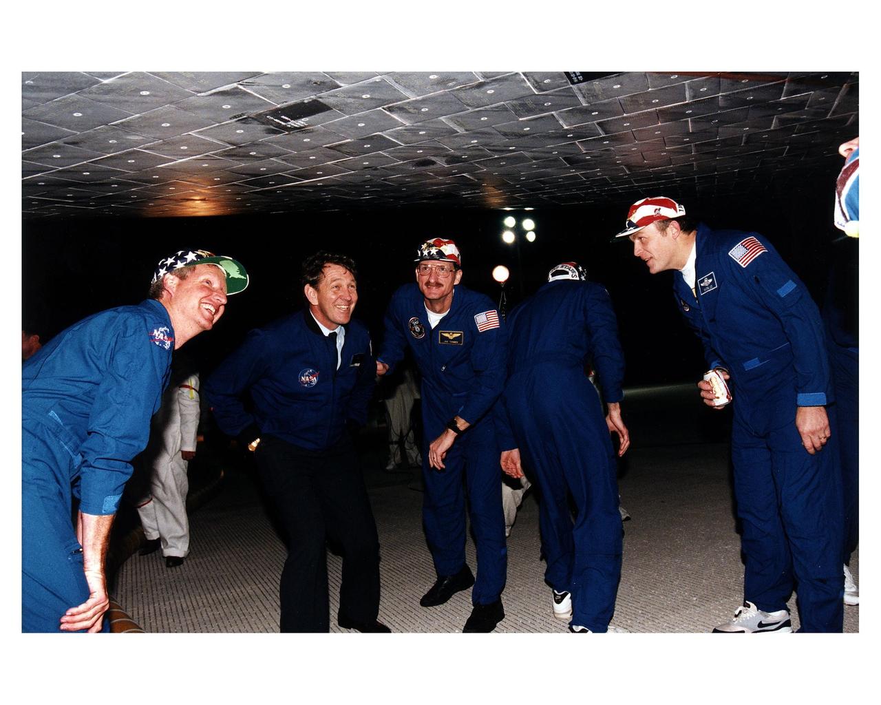 Accompanied by former astronaut Michael J. McCulley, several members of the STS-82 crew look at thermal protection system tile under the Space Shuttle Discovery on the runway at the Shuttle Landing Facility shortly after the conclusion of a 10-day mission to service the orbiting Hubble Space Telescope (HST). From left to right, they are Mission Specialist Steven A. Hawley; Michael J. McCulley, currently vice president and associate program manager for ground operations for the United Space Alliance at KSC; Mission Specialists Joseph R. "Joe" Tanner and Steven L. Smith (back to camera); and Payload Commander Mark C. Lee. STS-82 is the ninth Shuttle nighttime landing, and the fourth nighttime landing at KSC. The seven-member crew performed a record-tying five back-to-back extravehicular activities (EVAs) or spacewalks to service the telescope, which has been in orbit for nearly seven years. Two new scientific instruments were installed, replacing two outdated instruments. Five spacewalks also were performed on the first servicing mission, STS-61, in December 1993. Only four spacewalks were scheduled for STS-82, but a fifth one was added during the flight to install several thermal blankets over some aging insulation covering three HST compartments containing key data processing, electronics and scientific instrument telemetry packages. STS-82 was the 82nd Space Shuttle flight and the second mission of 1997