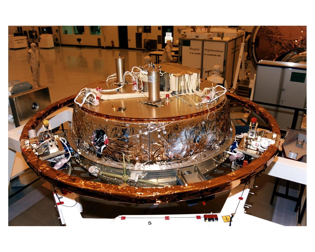 The descent module of the Titan-bound Huygens probe undergoes preflight processing on a support structure in the Payload Hazardous Servicing Facility (PHSF). The probe will study the clouds, atmosphere and surface of Saturn's moon, Titan, as part of the Cassini mission to the Saturnian system. The cylinders on the top of the probe contain antennas; the small square box has a parachute. The probe will detach from the Cassini orbiter after arrival at Saturn in 2004 to slowly descend through Titan's atmosphere to the surface of the Saturn moon. The Cassini launch on a Titan IVB/Centaur expendable launch vehicle is scheduled for October 6 from Cape Canaveral Air Station