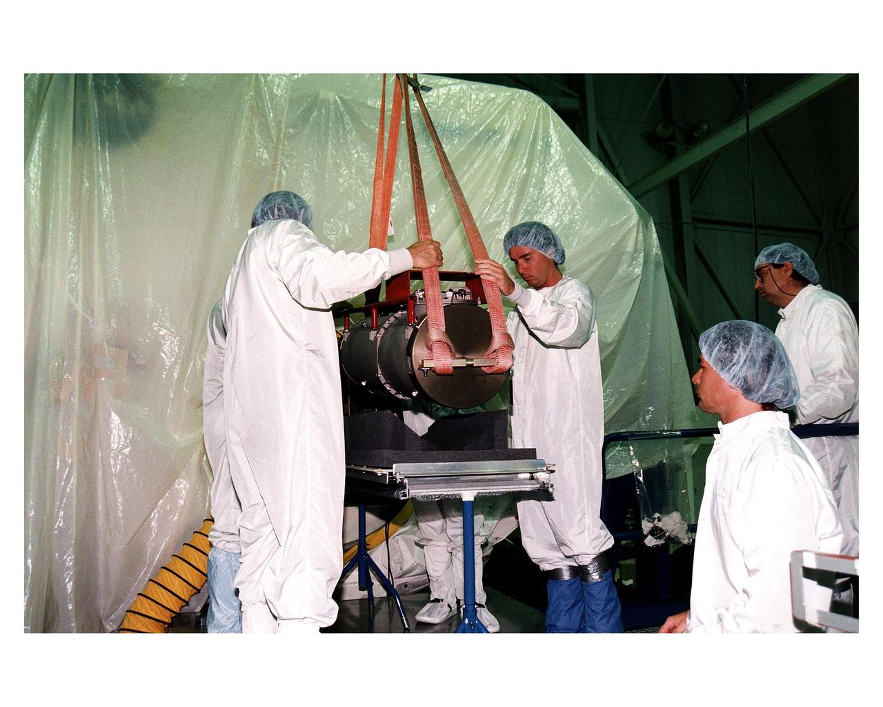 KENNEDY SPACE CENTER, FLA. -- McDonnell Douglas-SPACEHAB technicians oversee the move of a Russian-made oxygen generator to a SPACEHAB Double Module, at rear, in the SPACEHAB Payload Processing Facility. With faces visible in center foreground, from left, are Mark Halavin and Marc Tuttle; Mike Vawter is at far right. The oxygen generator, manufactured in Russia by RSC Energia, will be carried aboard the Space Shuttle Atlantis on Mission STS-84 for the Shuttle’s scheduled docking with the Russian Space Station Mir next month. The nearly 300-pound generator will replace one of two Mir units that have been malfunctioning recently. The generator functions by electrolysis, which separates water into its oxygen and hydrogen components. The hydrogen is vented and the oxygen is used for breathing by the Mir crew. The generator is 4.2 feet in length and 1.4 feet in diameter. STS-84, which is planned to include a Mir crew exchange of astronaut C. Michael Foale for Jerry M. Linenger, is targeted for a May 15 liftoff. It will be the sixth Shuttle-Mir docking