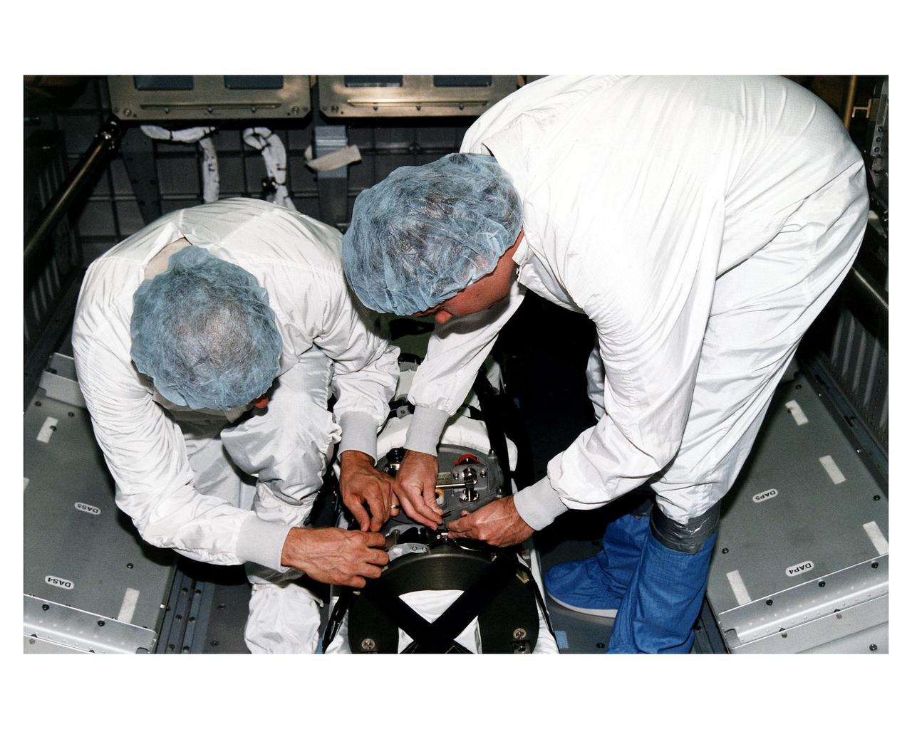 KENNEDY SPACE CENTER, FLA. -- McDonnell Douglas-SPACEHAB technicians strap in place a Russian-made oxygen generator on the floor of a SPACEHAB Double Module, being prepared for flight in the SPACEHAB Payload Processing Facility. From left, are Mark Halavin and Marc Tuttle. The oxygen generator, manufactured in Russia by RSC Energia, will be carried aboard the Space Shuttle Atlantis on Mission STS-84 for the Shuttle’s scheduled docking with the Russian Space Station Mir next month. The nearly 300-pound generator will replace one of two Mir units that have been malfunctioning recently. The generator functions by electrolysis, which separates water into its oxygen and hydrogen components. The hydrogen is vented and the oxygen is used for breathing by the Mir crew. The generator is 4.2 feet in length and 1.4 feet in diameter. STS-84, which is planned to include a Mir crew exchange of astronaut C. Michael Foale for Jerry M. Linenger, is targeted for a May 15 liftoff. It will be the sixth Shuttle-Mir docking