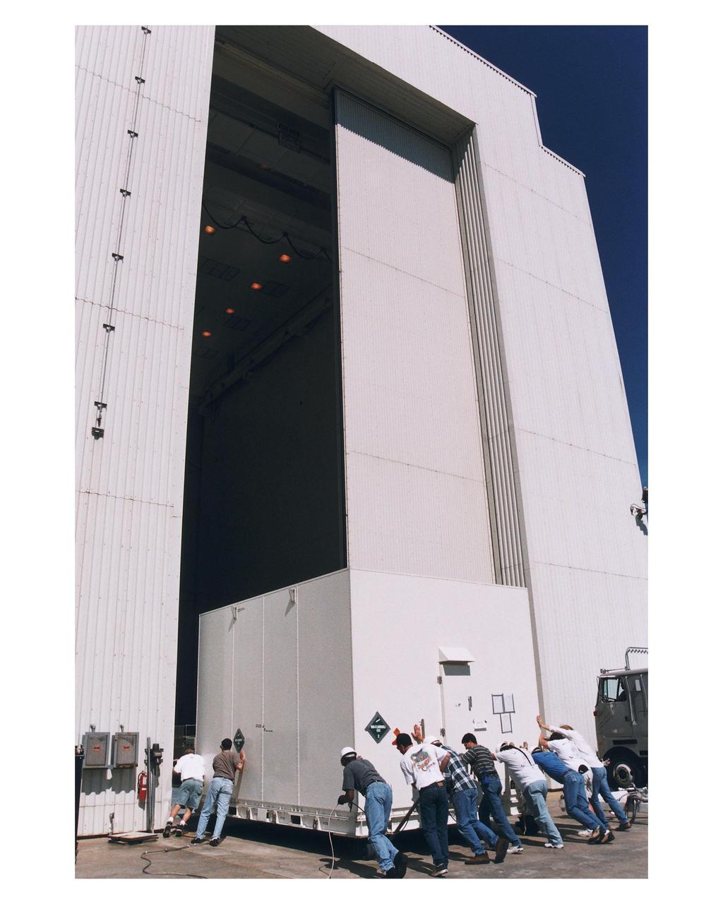 Workers prepare to move the shipping container with the Cassini orbiter inside the Payload Hazardous Servicing Facility (PHSF) for prelaunch processing, testing and integration. The <a href="http://www-pao.ksc.nasa.gov/kscpao/release/1997/66-97.htm">orbiter arrived</a> at KSC’s Shuttle Landing Facility in a U.S. Air Force C-17 air cargo plane from Edwards Air Force Base, California. The orbiter and the Huygens probe already being processed at KSC are the two primary components of the Cassini spacecraft, which will be launched on a Titan IVB/Centaur expendable launch vehicle from Cape Canaveral Air Station. Cassini will explore Saturn, its rings and moons for four years. The Huygens probe, designed and developed for the European Space Agency (ESA), will be deployed from the orbiter to study the clouds, atmosphere and surface of Saturn’s largest moon, Titan. The orbiter was designed and assembled at NASA’s Jet Propulsion Laboratory in California. Following postflight inspections, integration of the 12 science instruments not already installed on the orbiter will be completed. Then, the parabolic high-gain antenna and the propulsion module will be mated to the orbiter, followed by the Huygens probe, which will complete spacecraft integration. The Cassini mission is targeted for an Oct. 6 launch to begin its 6.7-year journey to the Saturnian system. Arrival at the planet is expected to occur around July 1, 2004