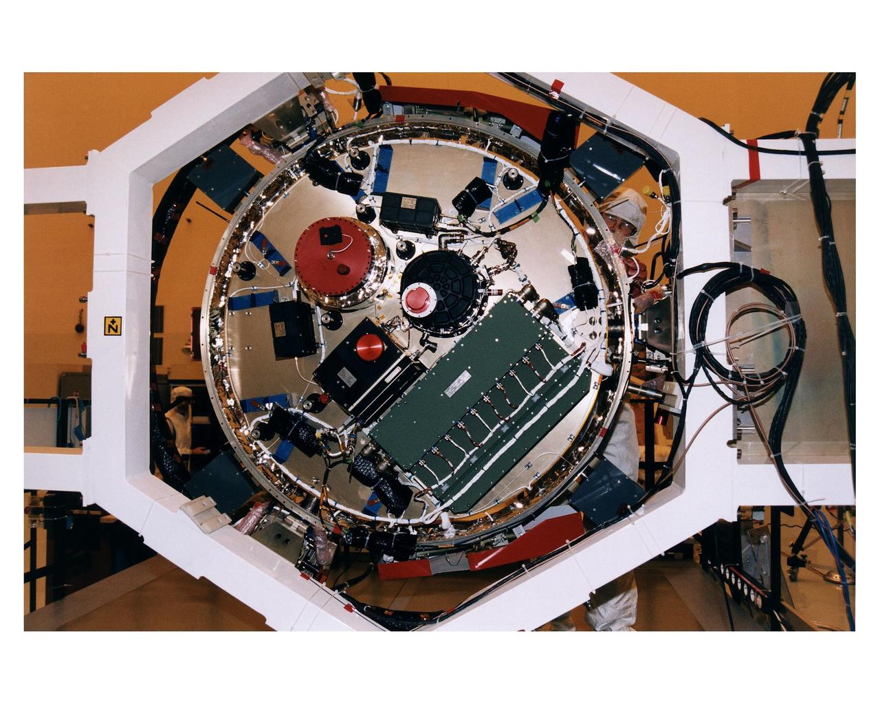 A worker in the Payload Hazardous Servicing Facility (PHSF) stands behind the bottom side of the experiment platform for the Huygens probe that will accompany the Cassini orbiter to Saturn during prelaunch processing testing and integration in that facility. The Huygens probe and the Cassini orbiter being processed at KSC are the two primary components of the Cassini spacecraft, which will be launched on a Titan IVB/Centaur expendable launch vehicle from Cape Canaveral Air Station. Cassini will explore Saturn, its rings and moons for four years. The Huygens probe, designed and developed for the European Space Agency (ESA), will be deployed from the orbiter to study the clouds, atmosphere and surface of Saturn’s largest moon, Titan. The orbiter was designed and assembled at NASA’s Jet Propulsion Laboratory in California. Following postflight inspections, integration of the 12 science instruments not already installed on the orbiter will be completed. Then, the parabolic high-gain antenna and the propulsion module will be mated to the orbiter, followed by the Huygens probe, which will complete spacecraft integration. The Cassini mission is targeted for an Oct. 6 launch to begin its 6.7-year journey to the Saturnian system. Arrival at the planet is expected to occur around July 1, 2004