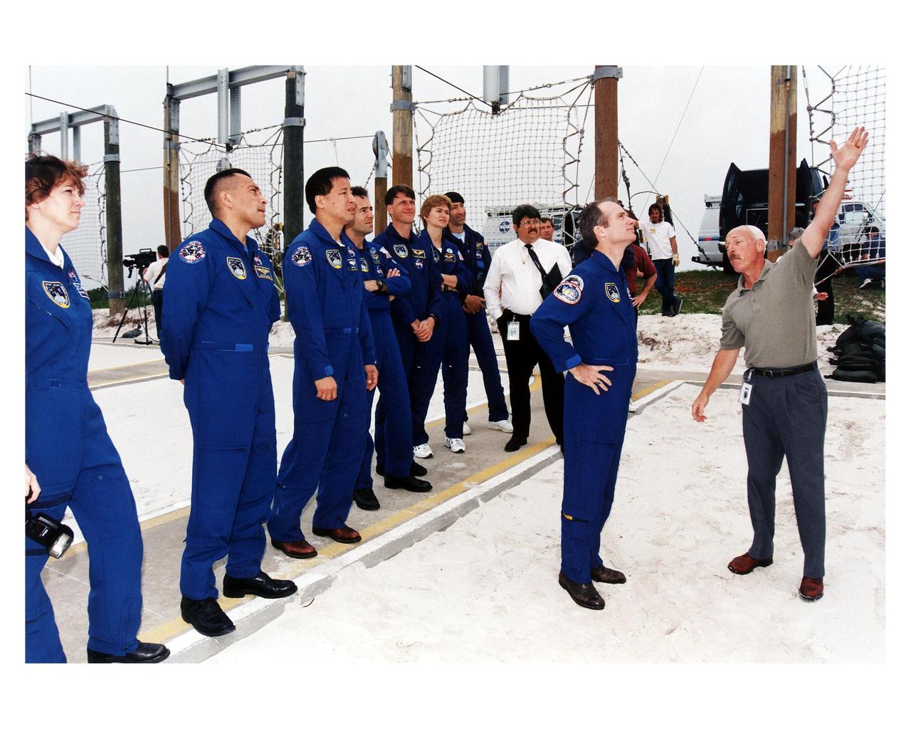 The STS-84 crew, with Commander Charles J. Precourt in front, gets instruction in Launch Pad 39A’s emergency egress system from Ken Clark, at right, a training instructor with United Space Alliance (USA). The sevenmember crew is participating in Terminal Countdown Demonstration Test (TCDT) activities. From left, are Pilot Eileen Marie Collins, and Mission Specialists Carlos I. Noriega, Edward Tsang Lu, Jean-Francois Clervoy of the European Space Agency, C. Michael Foale and Elena V. Kondakova of the Russian Space Agency. NASA astronaut Mario Runco Jr., next to Kondakova in a blue flight suit, is assisting the crew during TCDT. STS-84 will be the sixth docking of the Space Shuttle with the Russian Space Station Mir. After docking, Foale will transfer to the space station and become a member of the Mir 23 crew, replacing U.S. astronaut Jerry M. Linenger, who will return to Earth aboard Atlantis. Foale will live and work on Mir until mid-September when his replacement is expected to arrive on the STS-86 mission. STS-84 is targeted for a May 15 liftoff