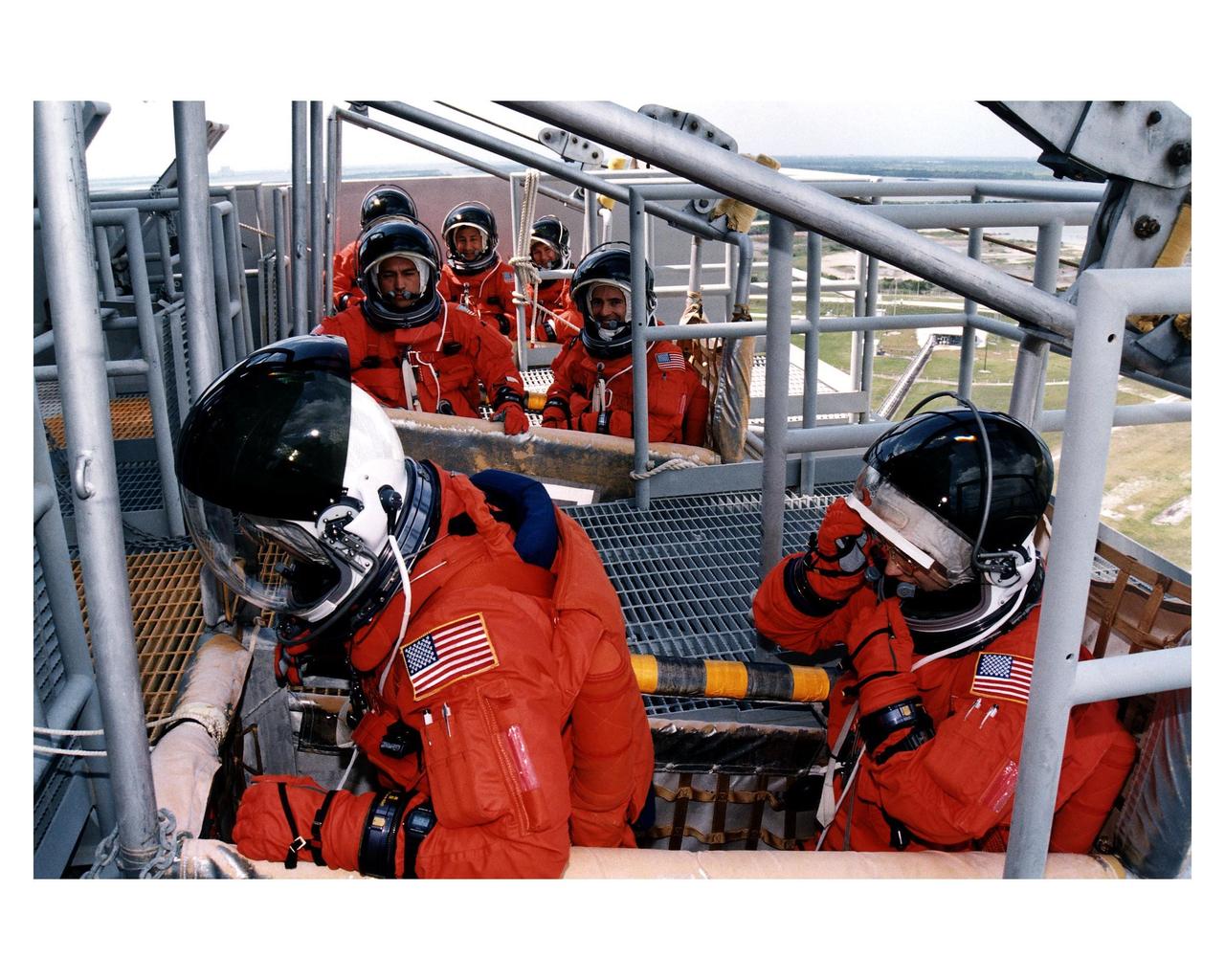 STS-84 crew members practice emergency egress procedures in slidewire baskets at Launch Pad 39A. They are participating in the Terminal Countdown Demonstration Test (TCDT), a dress rehearsal for launch. In the foreground are Commander Charles J. Precourt, at left, and Pilot Eileen Marie Collins. In the middle basket are Mission Specialists Carlos I. Noriega, at left, and Jean-Francois Clervoy of the European Space Agency. In the last slidewire basket at rear, from left, are Mission Specialists C. Michael Foale, Edward Tsang Lu and Elena V. Kondakova of the Russian Space Agency. STS-84 aboard Atlantis will be the sixth docking of the Space Shuttle with the Russian Space Station Mir. After docking, Foale will transfer to the space station and become a member of the Mir 23 crew, replacing U.S. astronaut Jerry M. Linenger, who will return to Earth aboard Atlantis. Foale will live and work on Mir until mid-September when his replacement is expected to arrive on the STS-86 mission. STS-84 is targeted for a May 15 liftoff