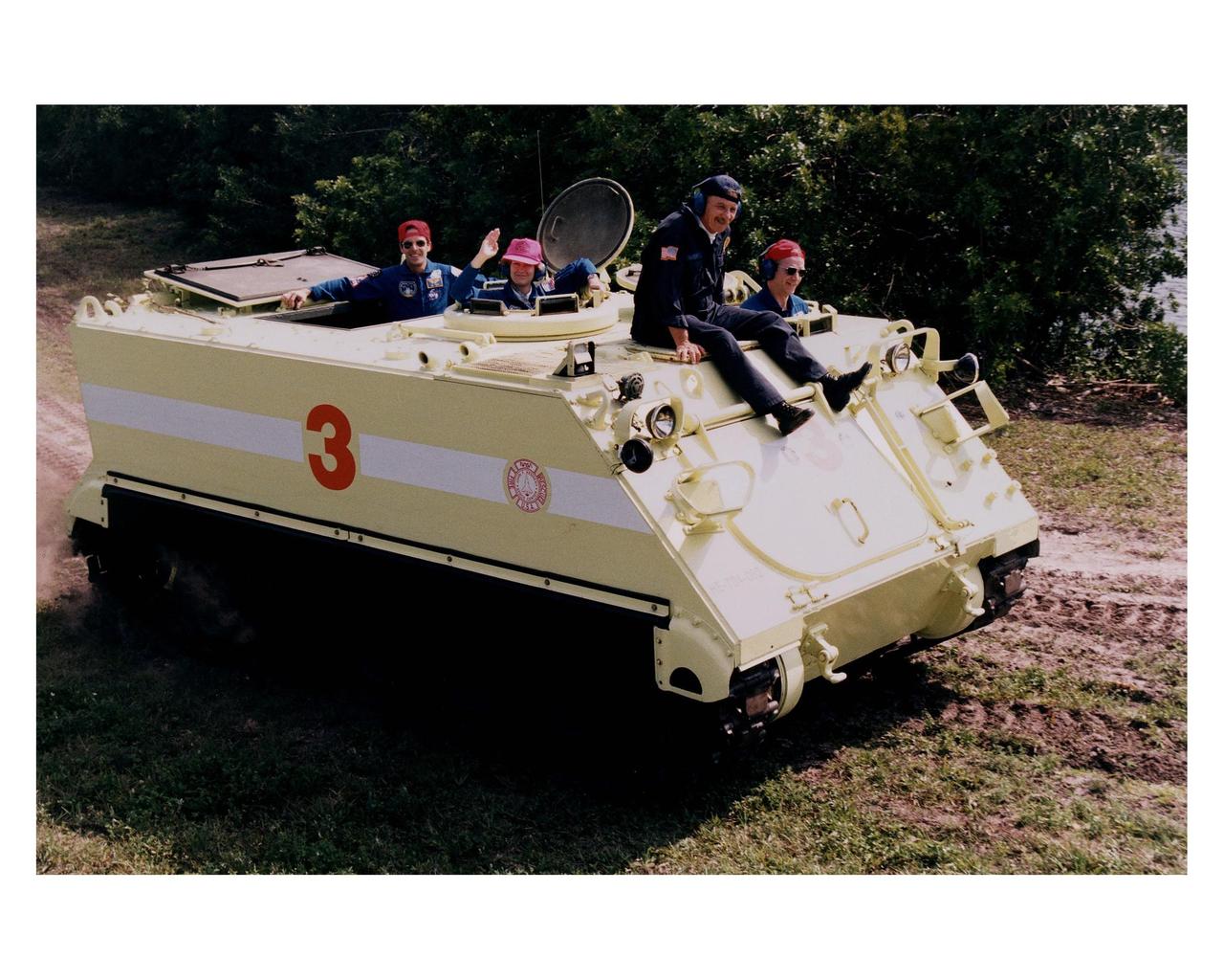 STS-84 crew members ride in and learn how to operate an M-113 armored personnel carrier as part of the Terminal Countdown Demonstration Test (TCDT) activities. Seated inside the M-113, from left, are Mission Specialist Jean-Francois Clervoy, Pilot Eileen Marie Collins (waving) and Commander Charles J. Precourt, in front. George Hoggard, a training officer with KSC Fire Services, sits on top of the personnel carrier. STS-84 aboard the Space Shuttle Atlantis will be the sixth docking of the Space Shuttle with the Russian Space Station Mir. After docking, STS-84 Mission Specialist C. Michael Foale will transfer to the space station and become a member of the Mir 23 crew, replacing U.S. astronaut Jerry M. Linenger, who will return to Earth aboard Atlantis. Foale will live and work on Mir until mid-September when his replacement is expected to arrive on the STS-86 mission. STS-84 is targeted for a May 15 liftoff