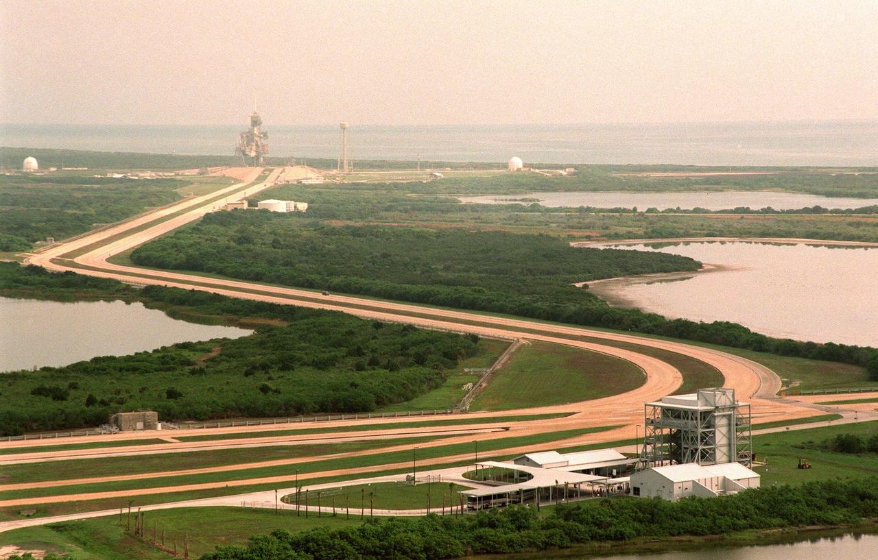 This aerial view looking northeast shows a new stop (bottom) on the KSC bus tour that allow visitors to view Pad LC-39B (top). The tour stop is next to the crawlerway that is used to transport the Space Shuttle vehicles to the pad. The length of the crawlerway from the Vehicle Assembly Building to Pad B is 6,828 meters (22,440 ft); its width overall is 40 meters (130 ft); each lane is 12 meters (40ft) with a 15-meter (50ft) median.