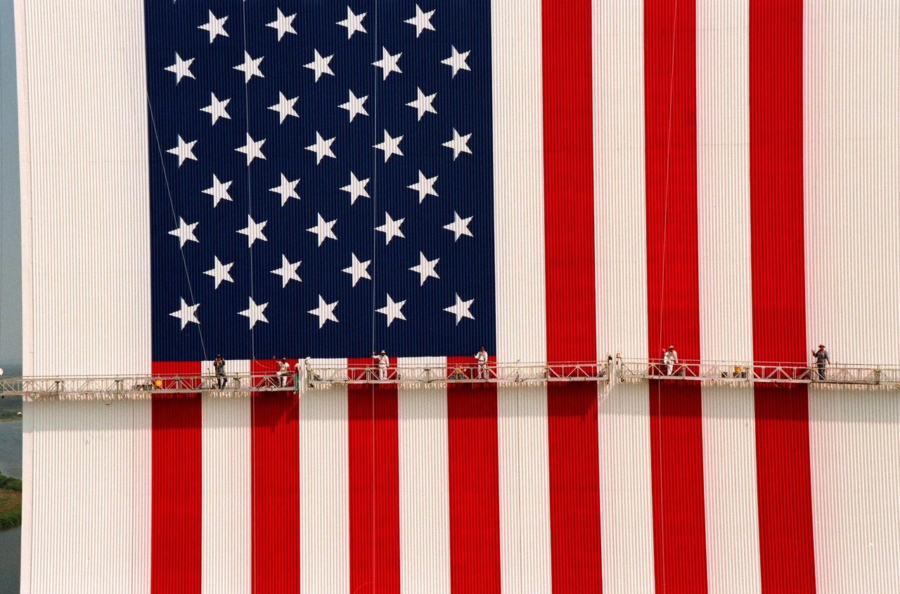 KENNEDY SPACE CENTER, FLA. -- This aerial view shows workers, suspended on platforms from the top of the 525-foot-high VAB, using rollers and brushes to repaint the flag on the Vehicle Assembly Building (VAB). The facelift honors NASA's 40th anniversary on Oct. 1 and is expected to be complete in mid-September. The flag spans an area 209 feet by 110 feet, or about 23,437 square feet. Each stripe is 9 feet wide and each star is 6 feet in diameter
