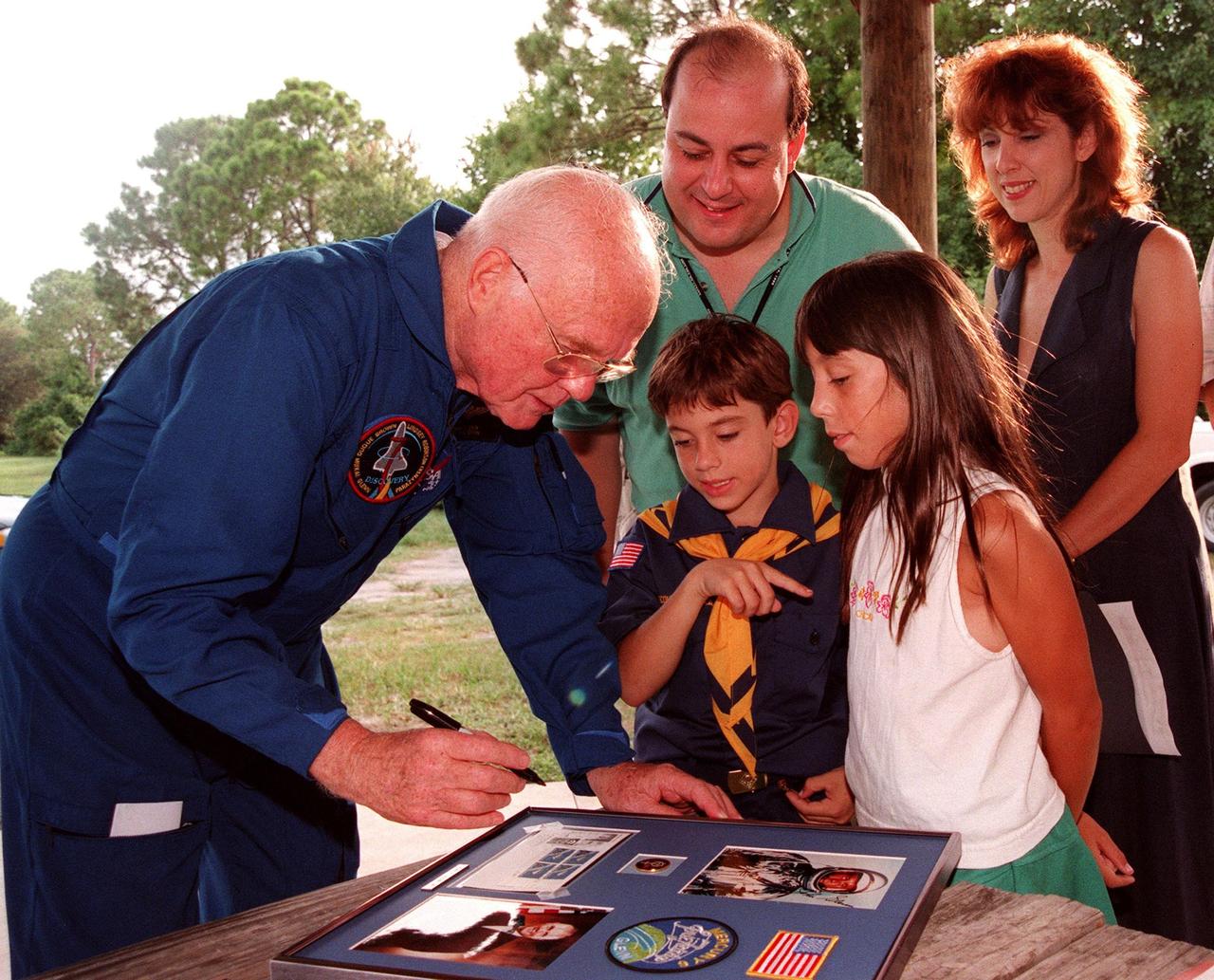 During a break in the Crew Equipment Interface Test (CEIT), Payload Specialist John H. Glenn Jr., a senator from Ohio, autographs a photo for Mathew and Alexandria Taraboletti. Standing behind them are their parents, Mark Taraboletti, an engineer with United Space Alliance (USA), and Eva Taraboletti, an orbiter integrity clerk with USA. The CEIT gives astronauts an opportunity for a hands-on look at the payloads and equipment with which they will be working on orbit. The launch of the STS-95 mission is scheduled for Oct. 29, 1998, on the Space Shuttle Discovery. The mission includes research payloads such as the Spartan solar-observing deployable spacecraft, the Hubble Space Telescope Orbital Systems Test Platform, the International Extreme Ultraviolet Hitchhiker, as well as the SPACEHAB single module with experiments on space flight and the aging process
