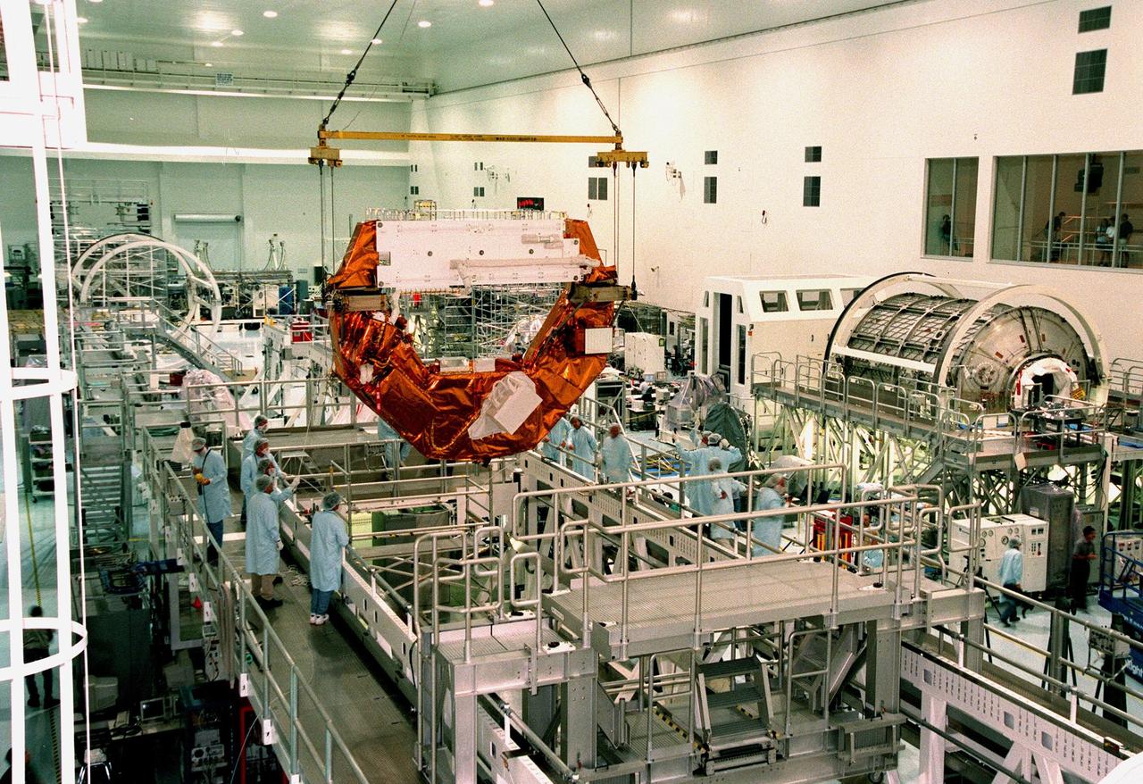 Workers watch as the Hubble Space Telescope Orbiting Systems Test (HOST)is lowered onto a workstand in the Space Shuttle Processing Facility. To the right can be seen the Rack Insertion Device and Leonardo, a Multi-Purpose Logistics Module. The HOST platform, one of the payloads on the STS-95 mission, is carrying four experiments to validate components planned for installation during the third Hubble Space Telescope servicing mission and to evaluate new technologies in an earth orbiting environment. The STS-95 mission is scheduled to launch Oct. 29. It will carry three other payloads: the Spartan solar-observing deployable spacecraft, the International Extreme Ultraviolet Hitchhiker, and the SPACEHAB single module with experiments on space flight and the aging process