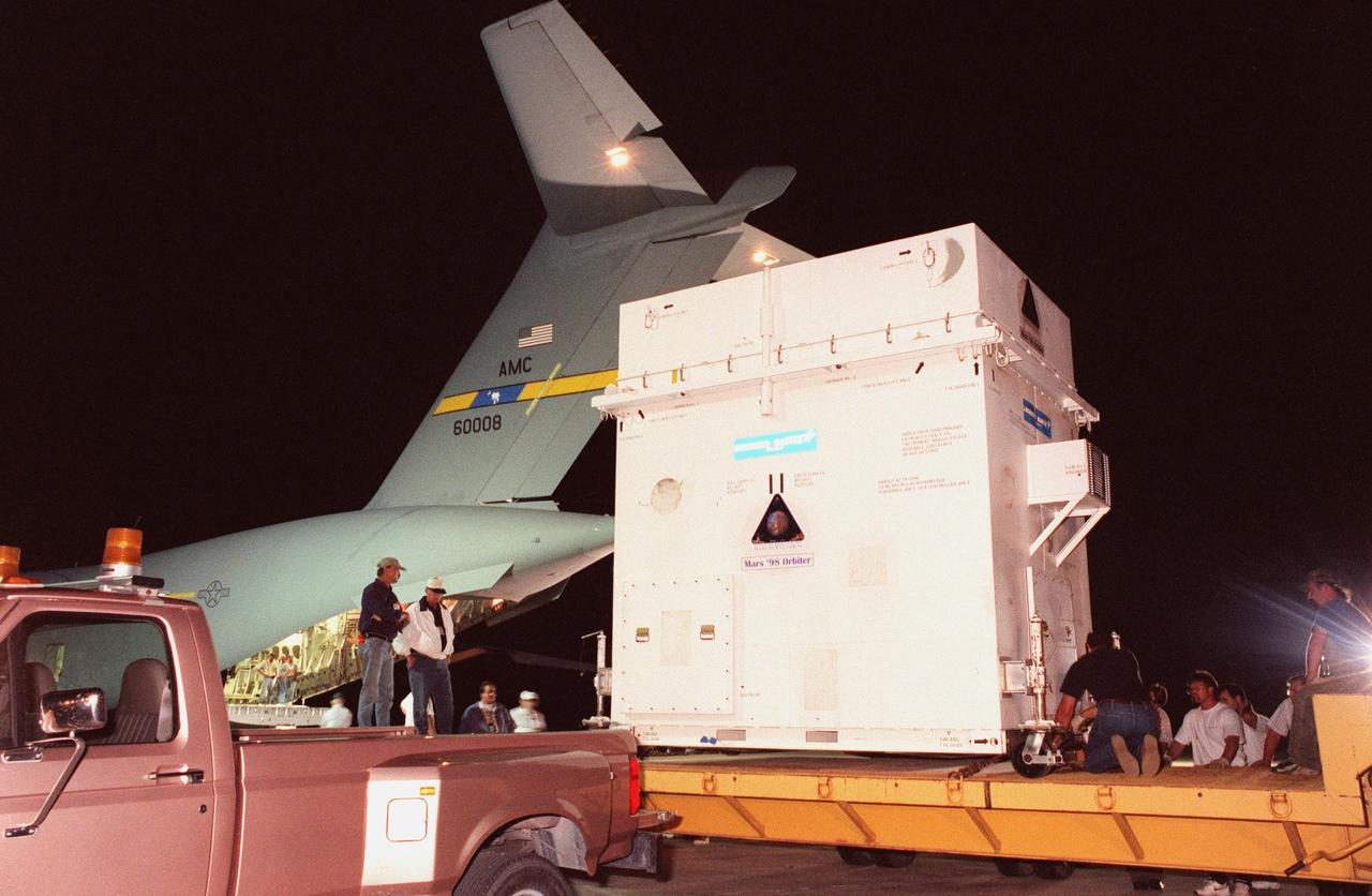 The Mars Climate Orbiter spacecraft is moved onto a flatbed for transport to the Spacecraft Assembly and Encapsulation Facility-2 (SAEF-2). It arrived at KSC's Shuttle Landing Facility aboard an Air Force C-17 cargo plane early this morning following its flight from the Lockheed Martin Astronautics plant in Denver, Colo. When it arrives at the red planet, the Mars Climate Orbiter will primarily support its companion Mars Polar Lander spacecraft, planned for launch on Jan. 3, 1999. After that, the Mars Climate Orbiter's instruments will monitor the Martian atmosphere and image the planet's surface on a daily basis for one Martian year (1.8 Earth years). It will observe the appearance and movement of atmospheric dust and water vapor, as well as characterize seasonal changes on the surface. The detailed images of the surface features will provide important clues to the planet's early climate history and give scientists more information about possible liquid water reserves beneath the surface. The scheduled launch date for the Mars Climate Orbiter is Dec. 10, 1998, on a Delta II 7425 rocket