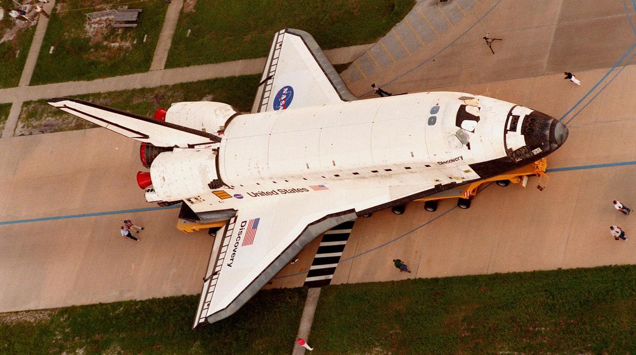 KSC employees accompany the orbiter Discovery on its rollover from the Orbiter Processing Facility Bay 2 to the Vehicle Assembly Building. The orbiter displays the recently painted NASA logo, termed the "meatball," on its left wing and both sides of the fuselage. Discovery (OV-103) is scheduled for its 25th flight, from Launch Pad 39B, on Oct. 29, 1998, for the STS-95 mission