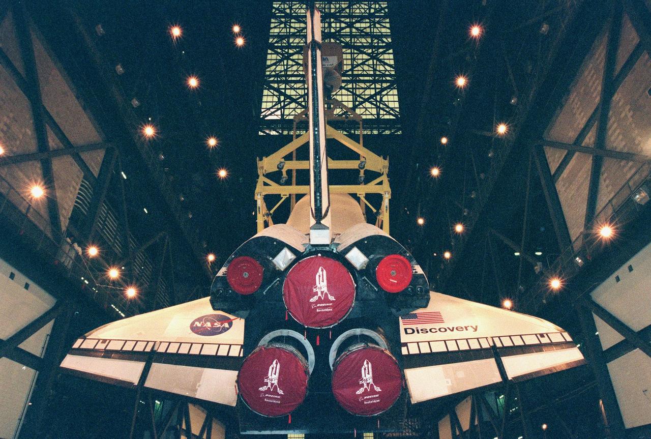 In the Vehicle Assembly Building, the orbiter Discovery (viewed from behind the Space Shuttle Main Engines) is raised to a vertical position in order to be mated with the external tank. The orbiter displays the recently painted NASA logo, termed the "meatball," on its left, or port, wing. The logo also has been painted on both sides of the aft fuselage. Discovery (OV-103), the first of the orbiters to be launched with the new art work, is scheduled for its 25th flight, from Launch Pad 39B, on Oct. 29, 1998, for the STS-95 mission