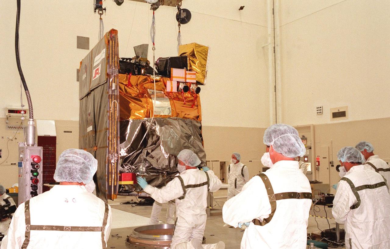 Technicians lower the Mars Climate Orbiter onto its workstand in the Spacecraft Assembly and Encapsulation Facility-2 (SAEF-2). The Mars Climate Orbiter is heading for Mars where it will primarily support its companion Mars Polar Lander spacecraft, planned for launch on Jan. 3, 1999. After that, the Mars Climate Orbiter's instruments will monitor the Martian atmosphere and image the planet's surface on a daily basis for one Martian year (two Earth years). It will observe the appearance and movement of atmospheric dust and water vapor, as well as characterize seasonal changes on the surface. The detailed images of the surface features will provide important clues to the planet's early climate history and give scientists more information about possible liquid water reserves beneath the surface. The scheduled launch date for the Mars Climate Orbiter is Dec. 10, 1998, on a Boeing Delta II 7425 rocket