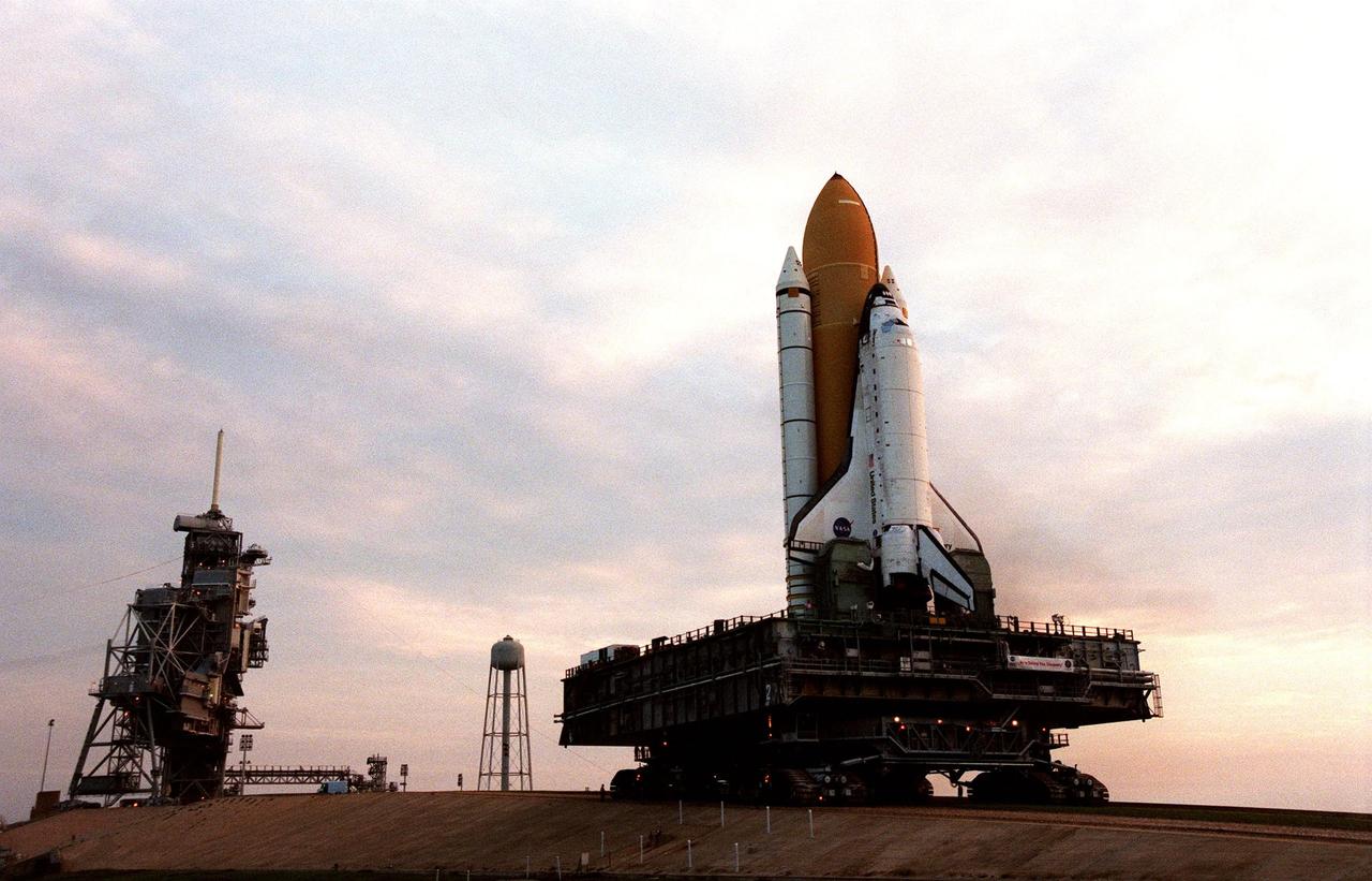 The early morning light reveals STS-95 Space Shuttle Discovery, on the Mobile Launch Platform, on its 6-hour, 4.2-mile trek to Launch Complex Pad 39B from the Vehicle Assembly Building. To the left is the Fixed Service Structure that provides access to the orbiter and the Rotating Service Structure. In the background is th eelevated water tank that helps reduce sound levels during launch. At the launch pad, the orbiter, external tank and solid rocket boosters will undergo final preparations for the launch, scheduled to lift off Oct. 29. The mission includes research payloads such as the Spartan solar-observing deployable spacecraft, the Hubble Space Telescope Orbital Systems Test Platform, the International Extreme Ultraviolet Hitchhiker, as well as the SPACEHAB single module with experiments on space flight and the aging process