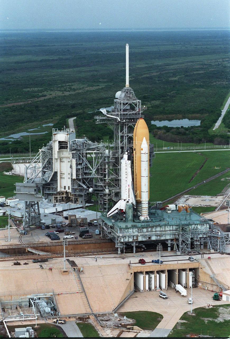 At the end of its 6-hour, 4.2-mile circular trek from the Vehicle Assembly Building, the STS-95 Space Shuttle Discovery, still on the Mobile Launch Platform and crawler transporter, sits at Launch Pad 39B. To its left is the Fixed Service Structure that provides access to the orbiter and the Rotating Service Structure. Above it is the 80-foot fiberglass lightning mast that provides protection from lightning strikes. The top of the photo looks west, across the Merritt Island National Wildlife Refuge. While at the launch pad, the orbiter, external tank and solid rocket boosters will undergo final preparations for the launch, scheduled to lift off Oct. 29. The mission includes research payloads such as the Spartan solar-observing deployable spacecraft, the Hubble Space Telescope Orbital Systems Test Platform, the International Extreme Ultraviolet Hitchhiker, as well as the SPACEHAB single module with experiments on space flight and the aging process